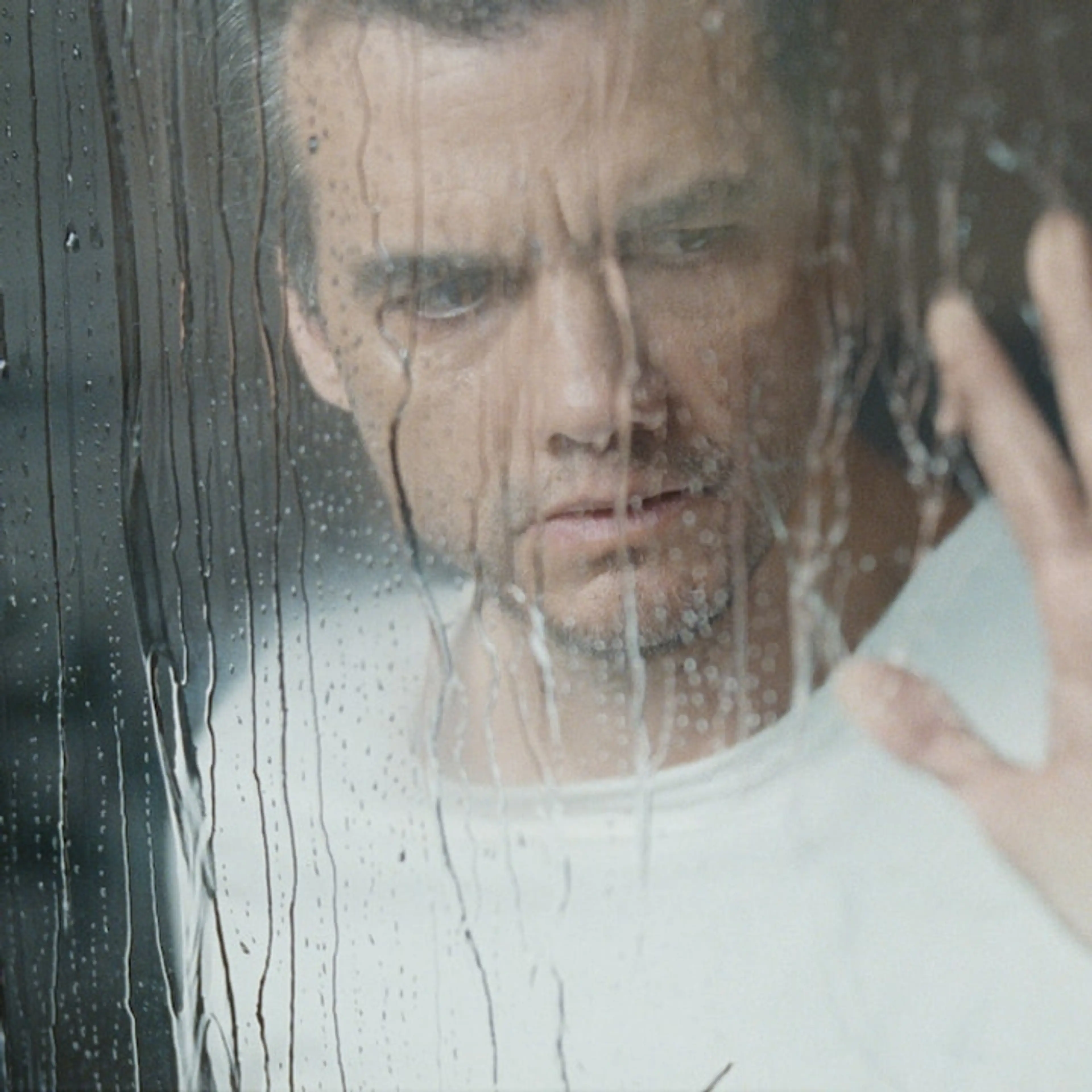 Wagner Moura as Jason behind a rain-streaked window in The Last House.