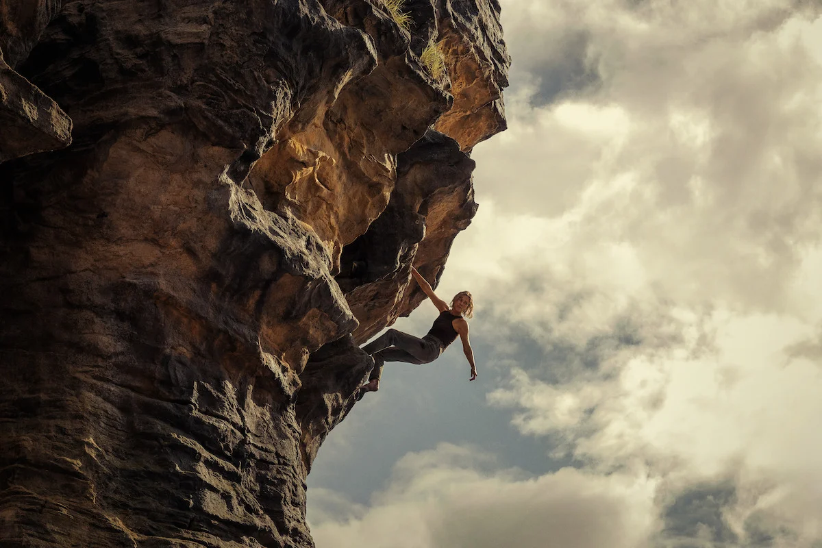 Sasha holds onto a steep overhanging rock face above a long drop.