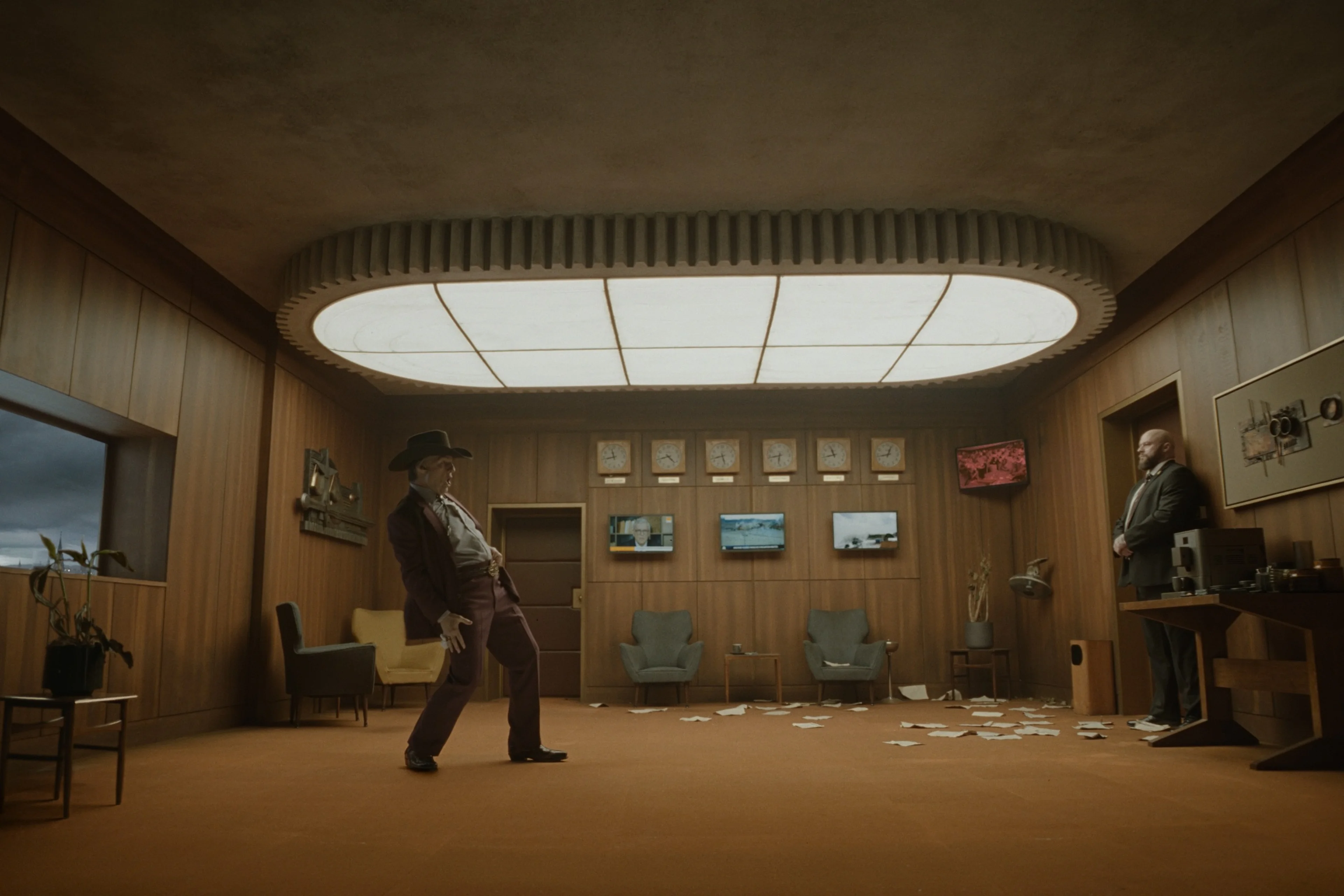 Two men stand apart in a large room with mounted animal heads and several screens in Digger.