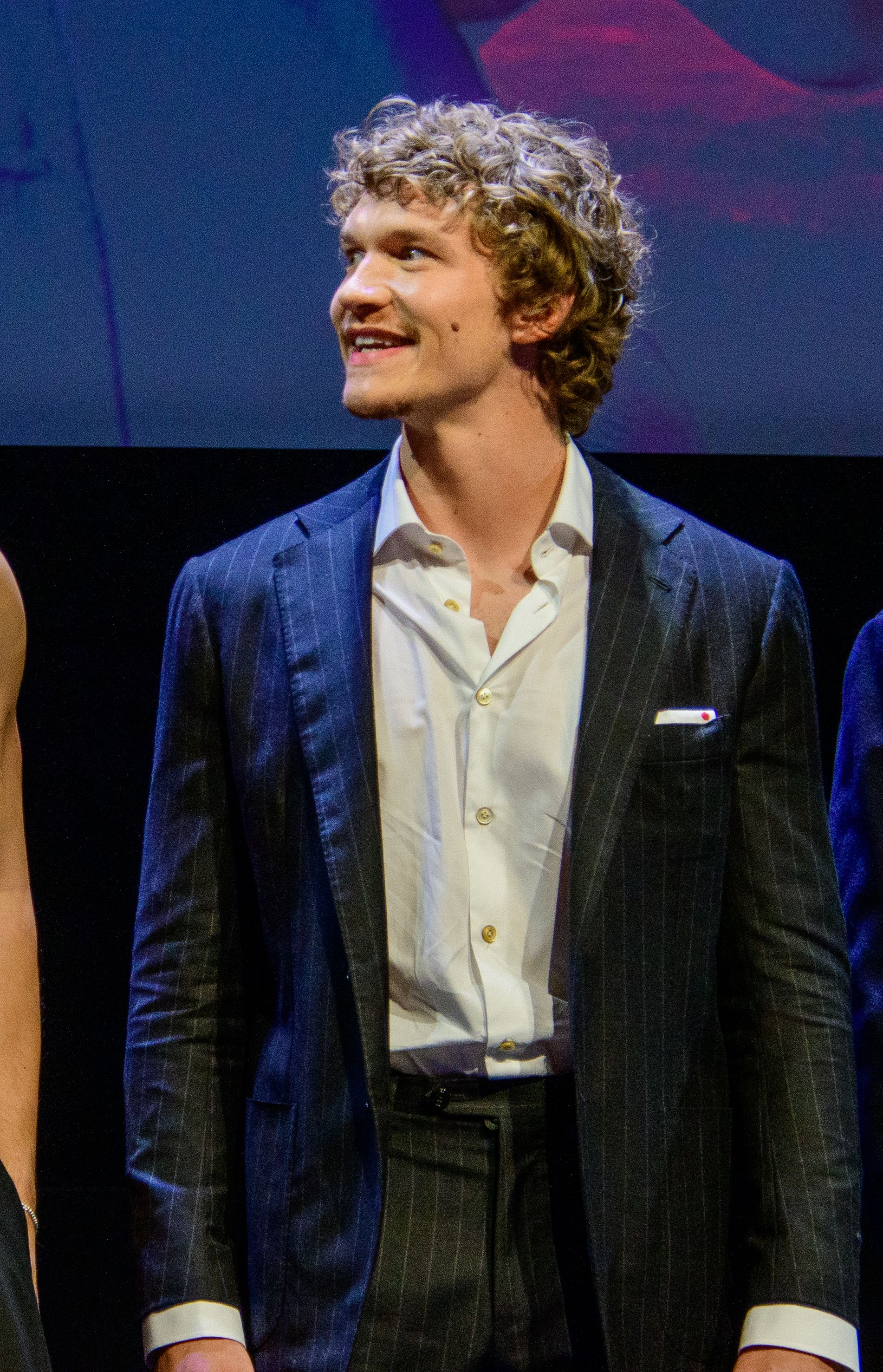 Connor Storrie at a public event, wearing a dark pinstripe suit.