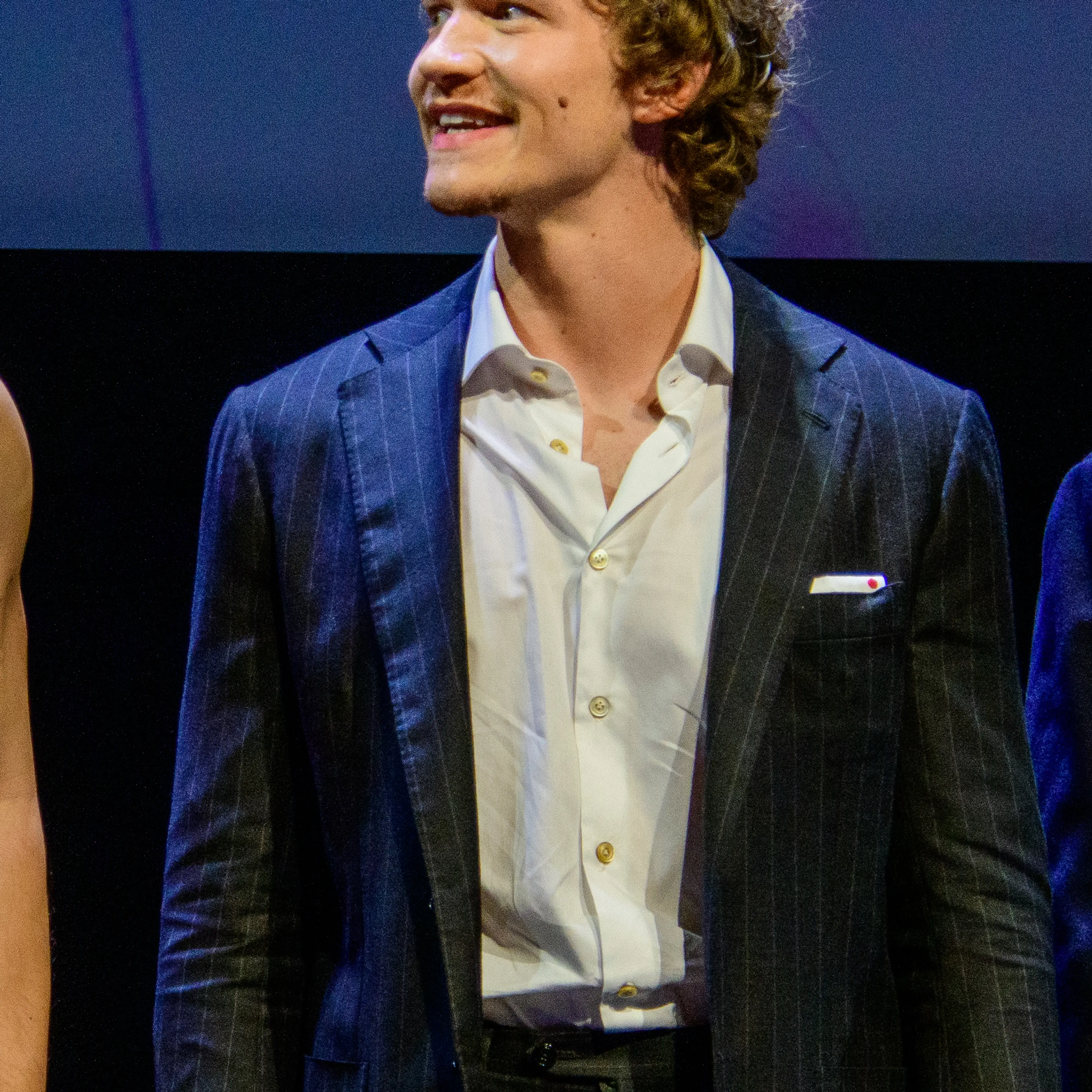 Connor Storrie at a public event, wearing a dark pinstripe suit.