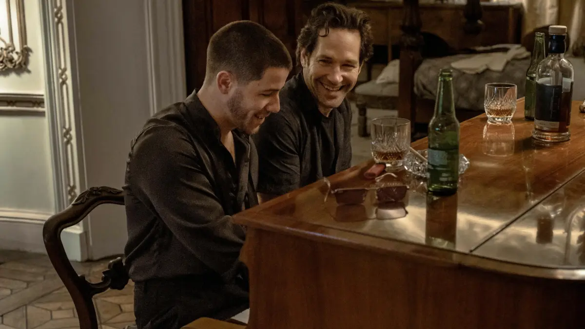 Danny and Rick smile beside a wooden piano with bottles on top.