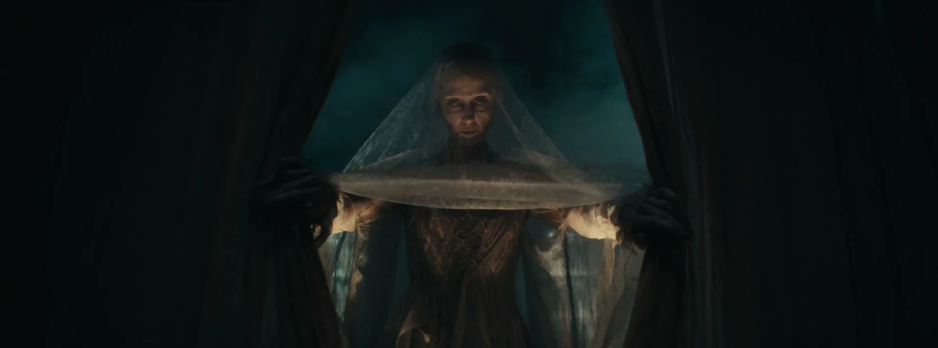 A pale veiled figure stands between the curtains of Scrooge’s bed.