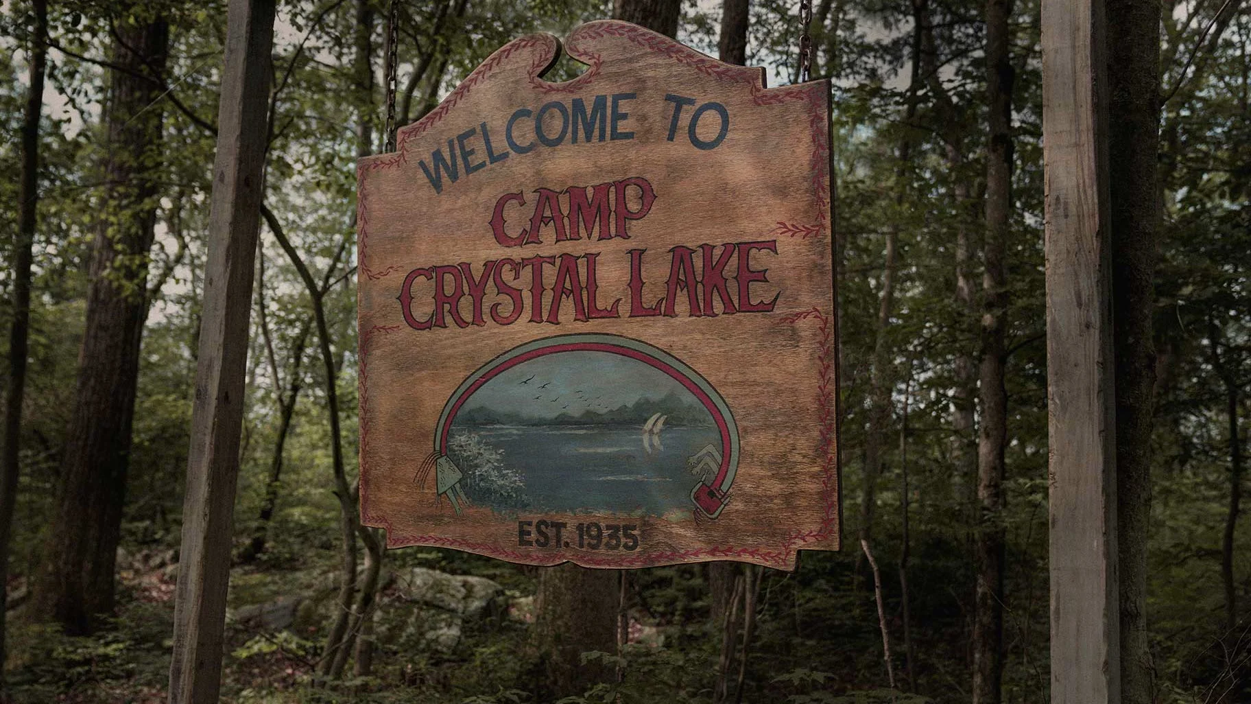 A wooden Welcome to Camp Crystal Lake sign stands beside a forest road.