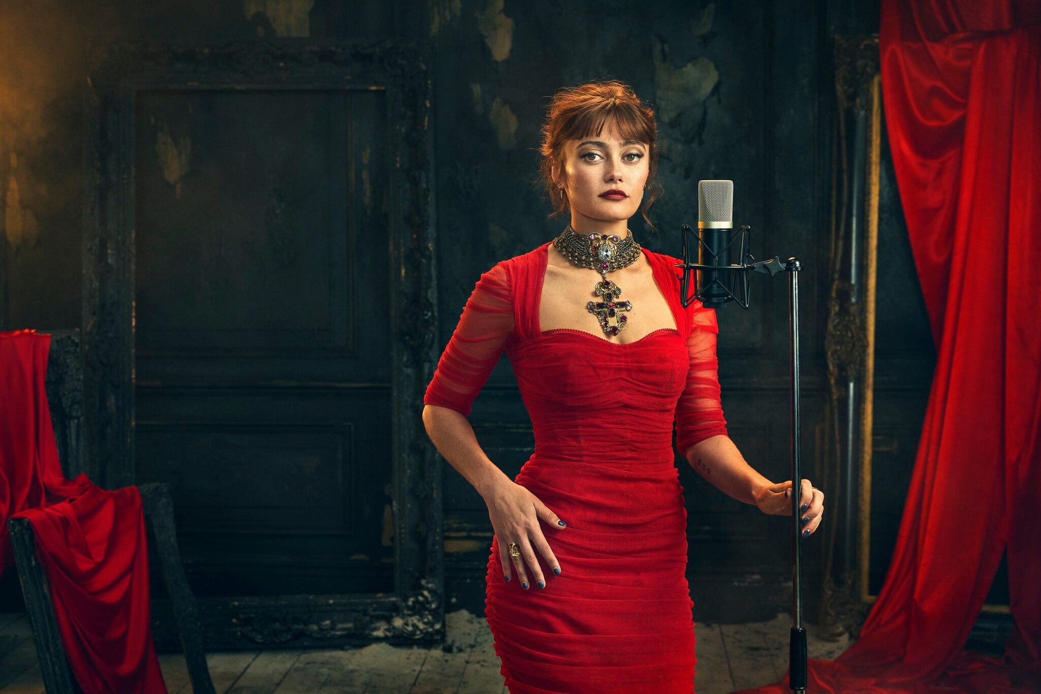 Ella Purnell wears a red dress beside a microphone in an official Dracula audio-drama portrait.