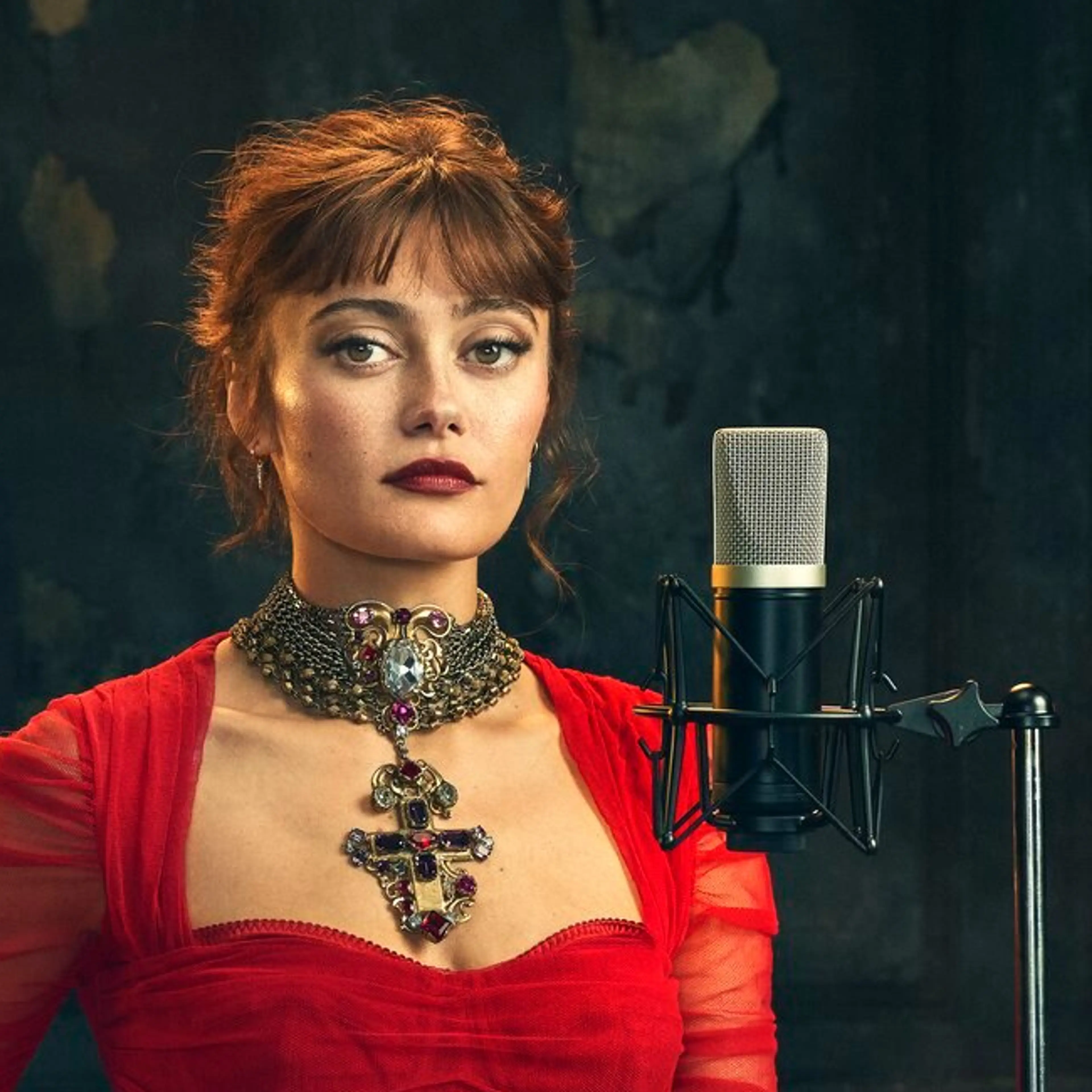 Ella Purnell wears a red dress beside a microphone in an official Dracula audio-drama portrait.