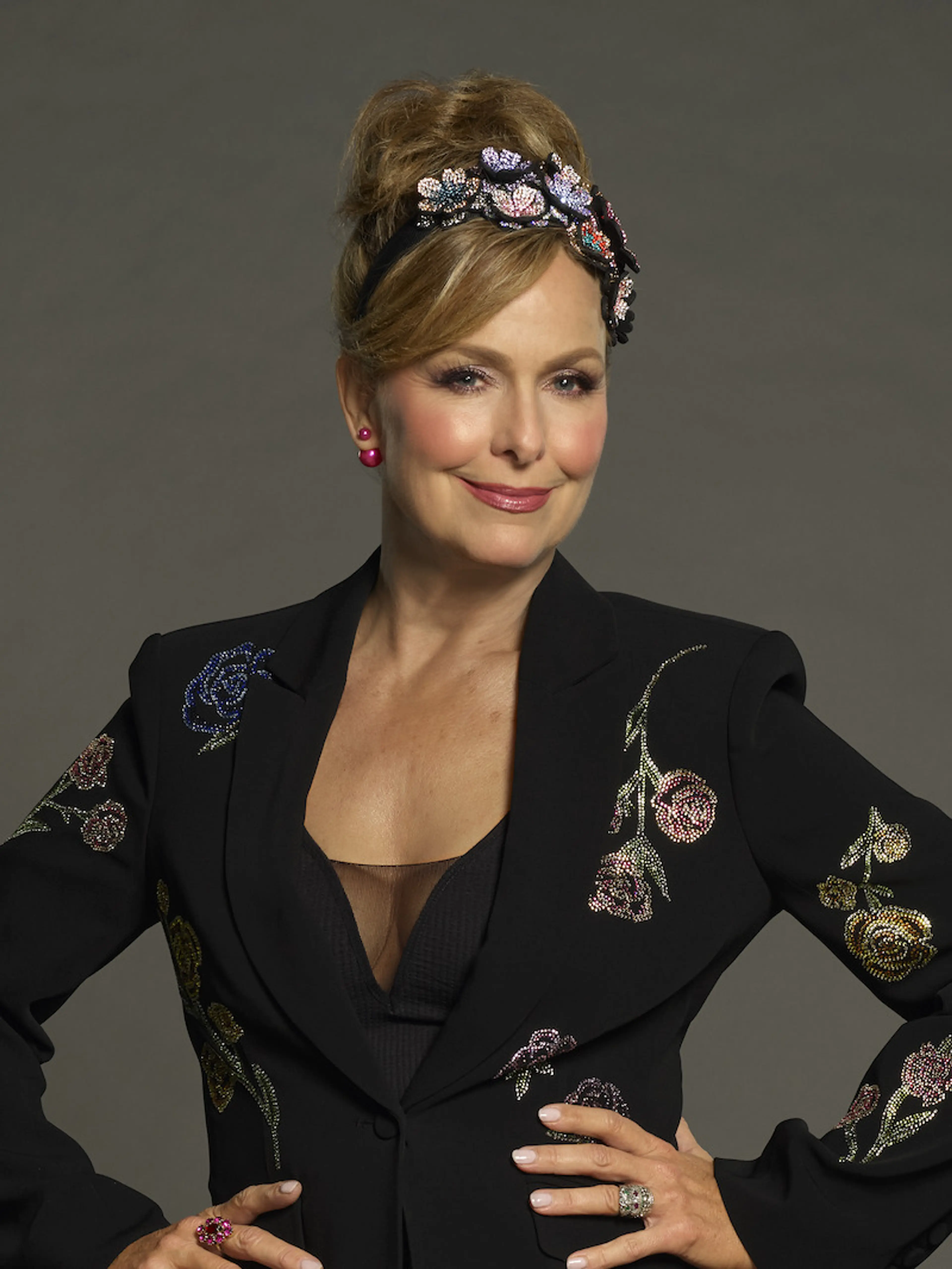 Melora Hardin poses in a black embroidered jacket and decorated headband for Celebrity Million Dollar Secret.
