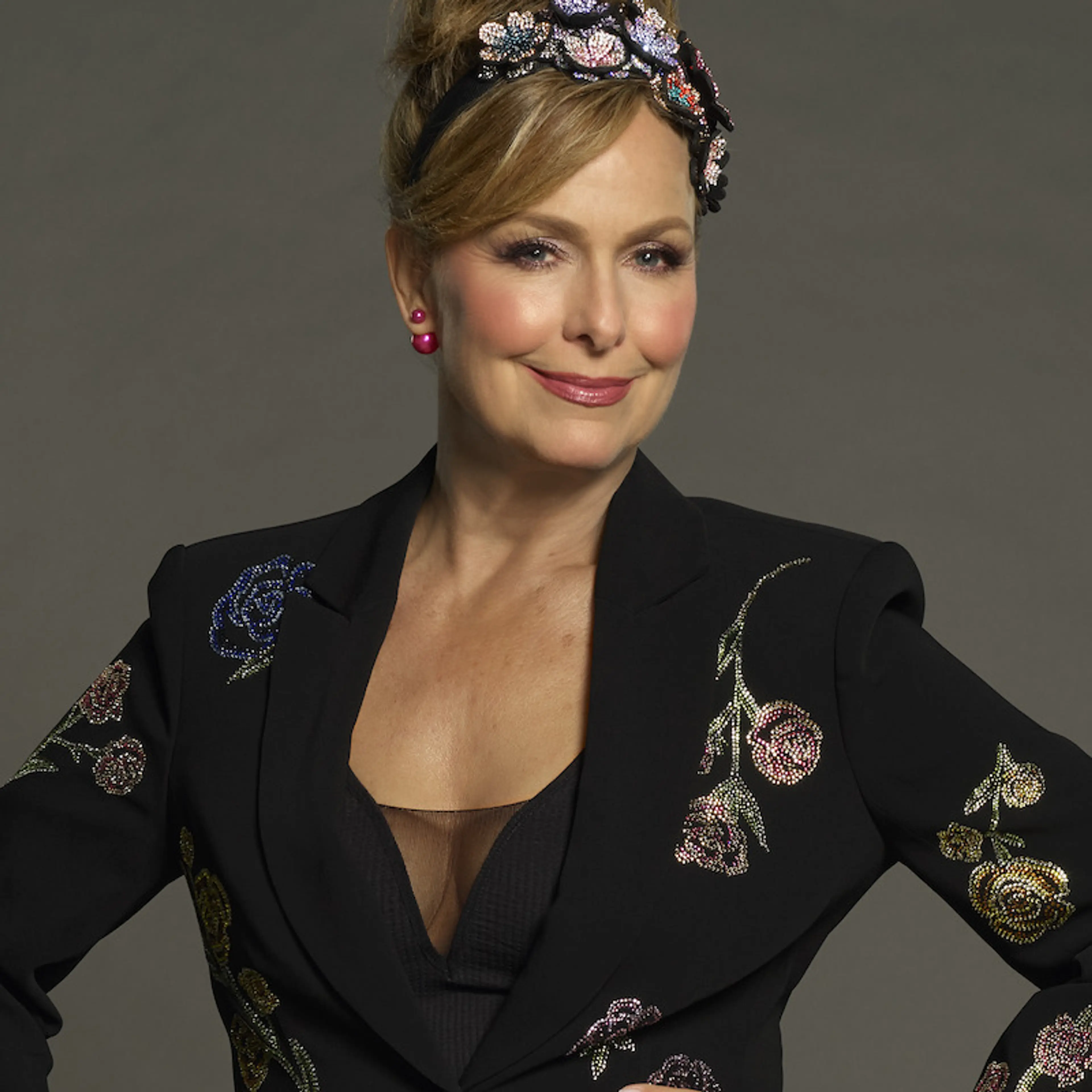 Melora Hardin poses in a black embroidered jacket and decorated headband for Celebrity Million Dollar Secret.