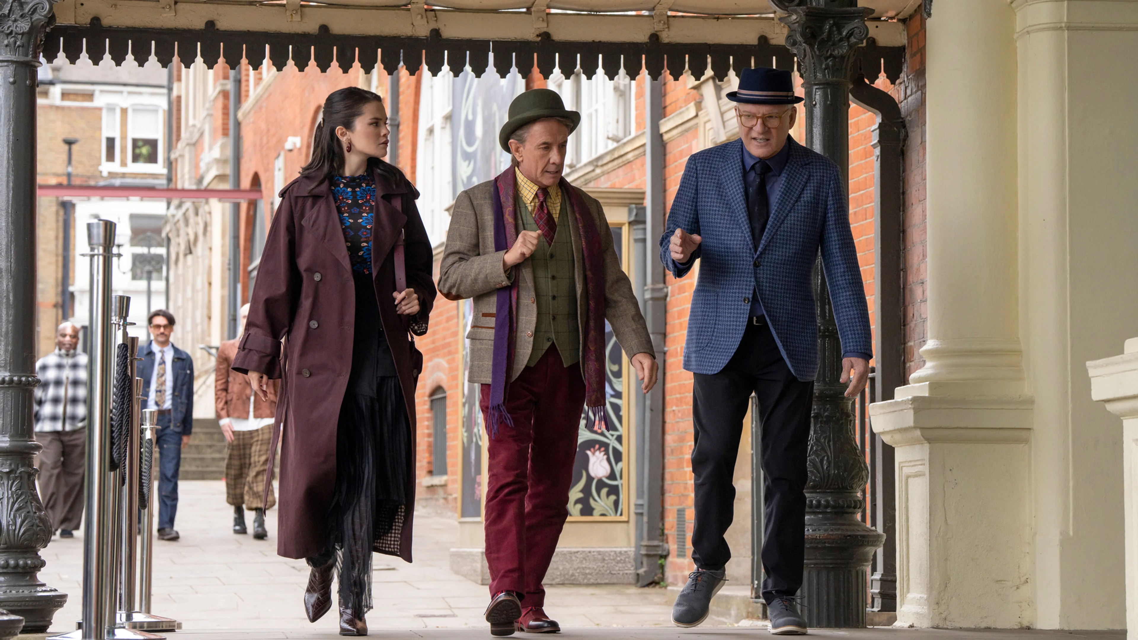 Charles, Mabel, and Oliver walk together under a covered walkway in London in an official Only Murders in the Building Season 6 still.