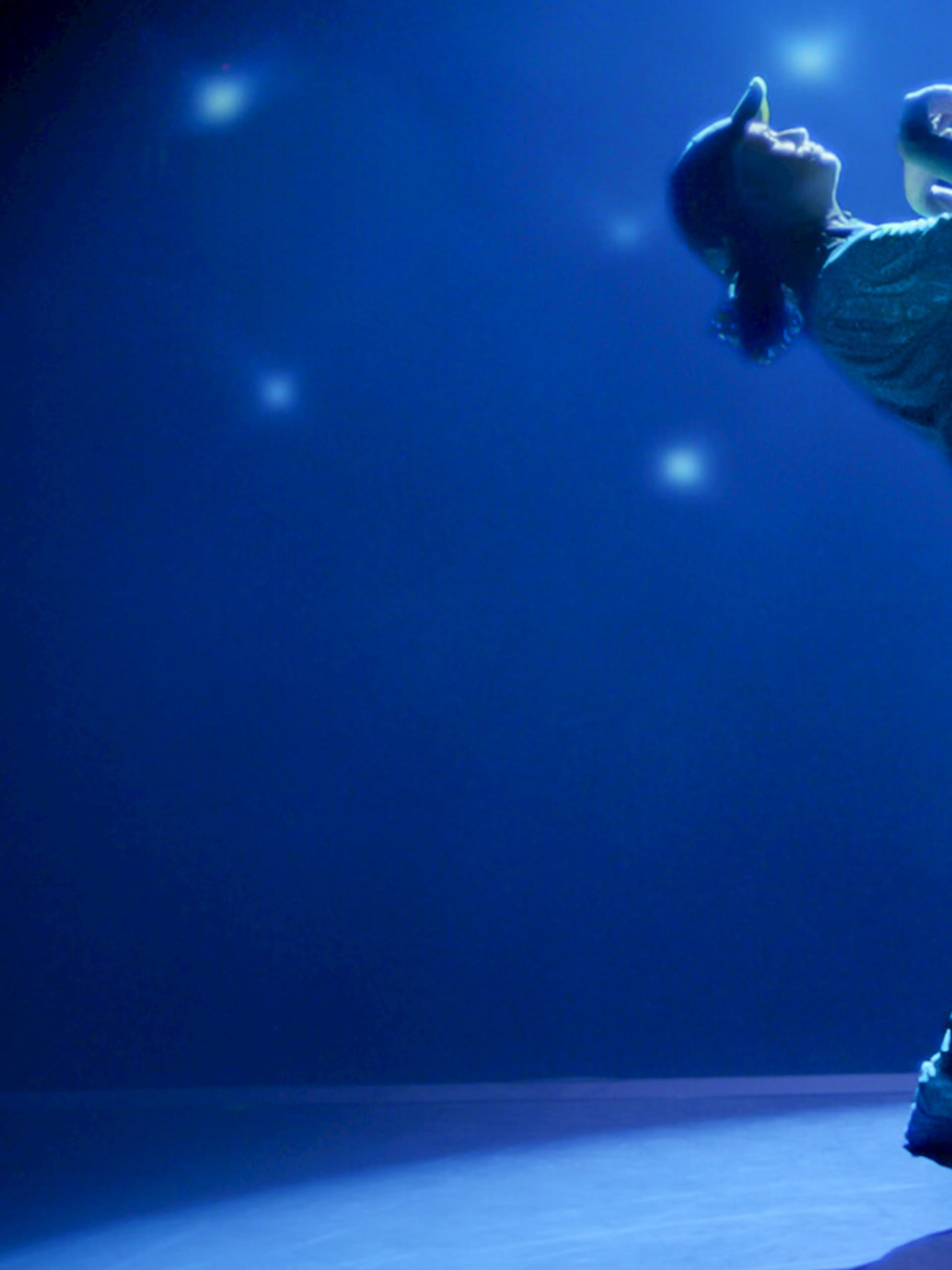 Rachael Gunn performs on a blue-lit stage in an official still from Untold Raygun: Breaking Badly.