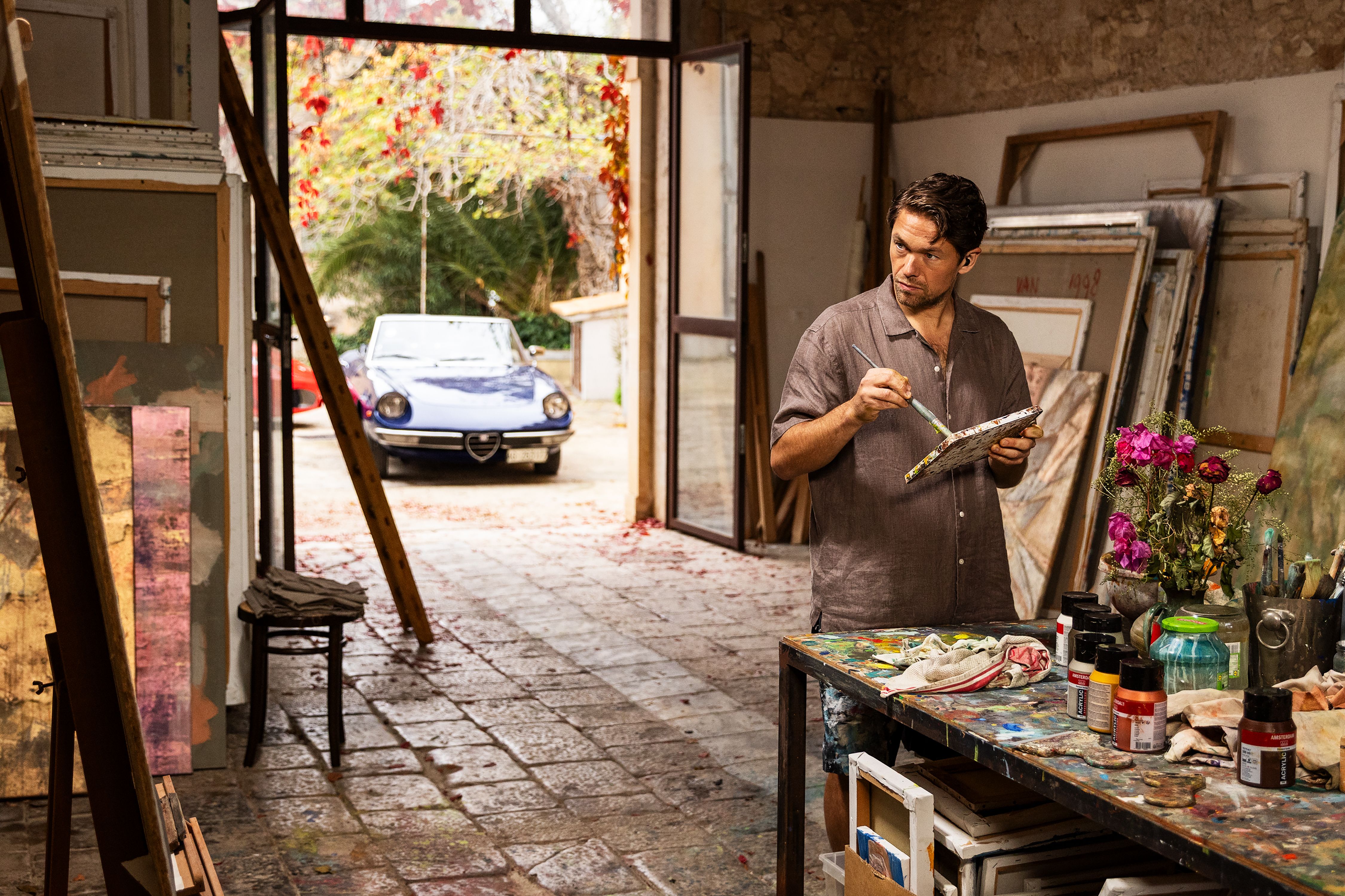 Jakob Oftebro as Adam stands beside a paint-covered table in an art studio in A Couple of Lies.