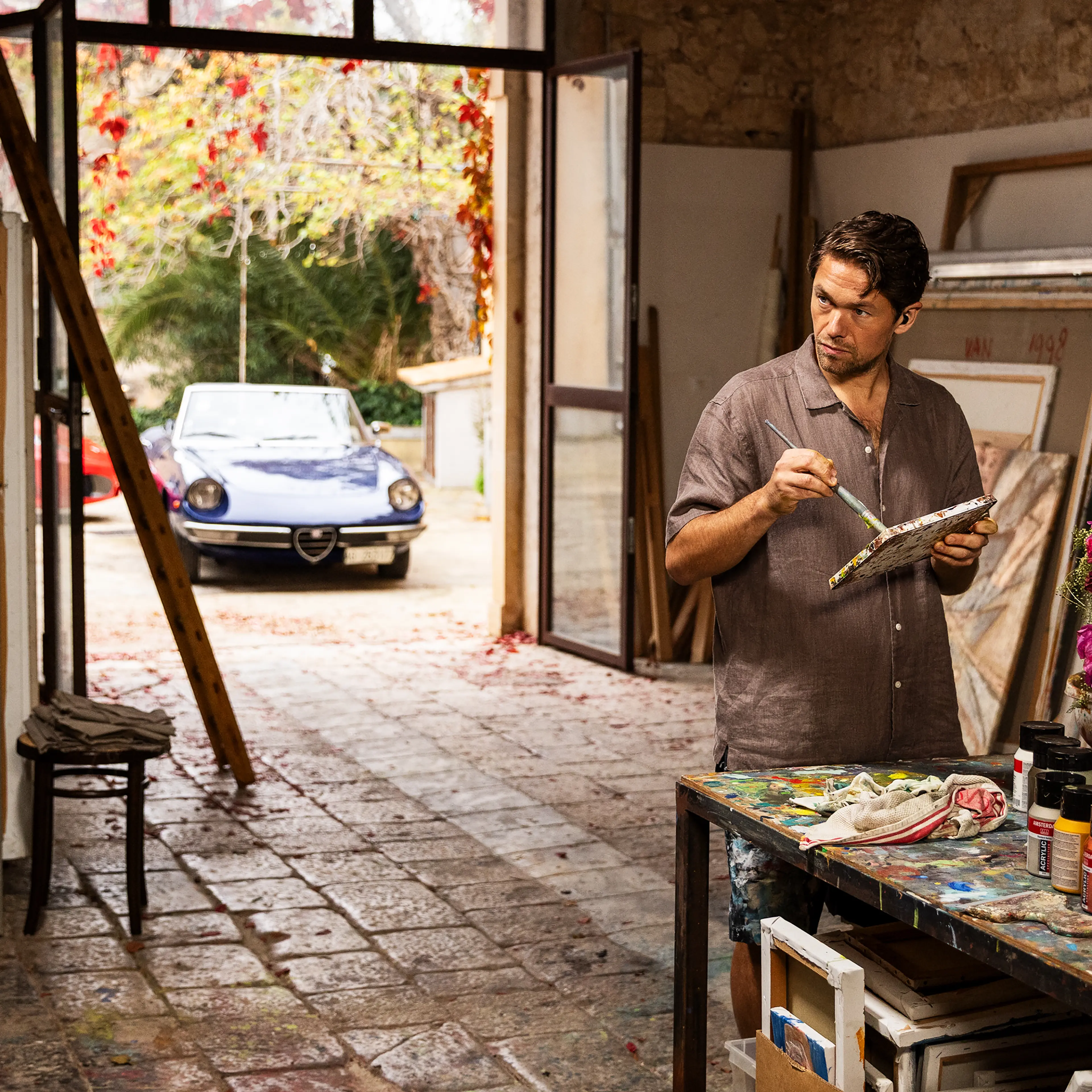 Jakob Oftebro as Adam stands beside a paint-covered table in an art studio in A Couple of Lies.