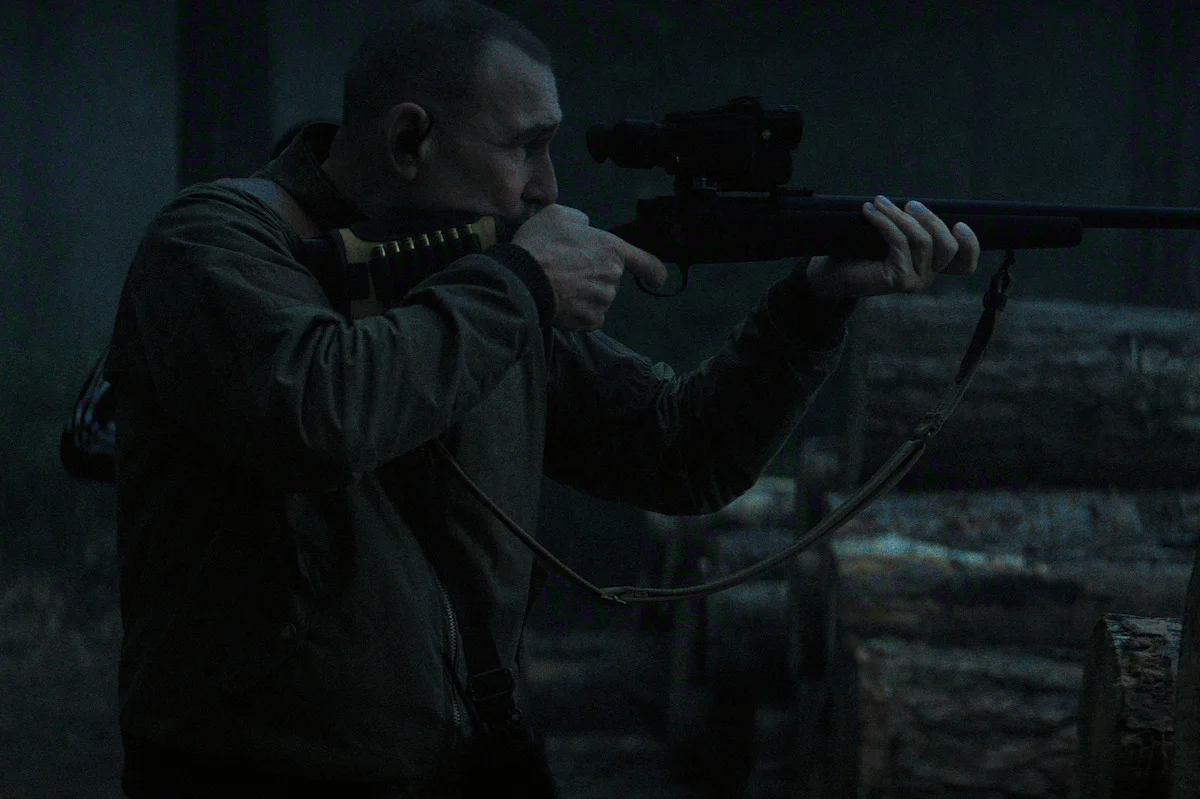 Vinnie Jones as Geoff aims a scoped rifle in a forest in The Gentlemen Season 2.