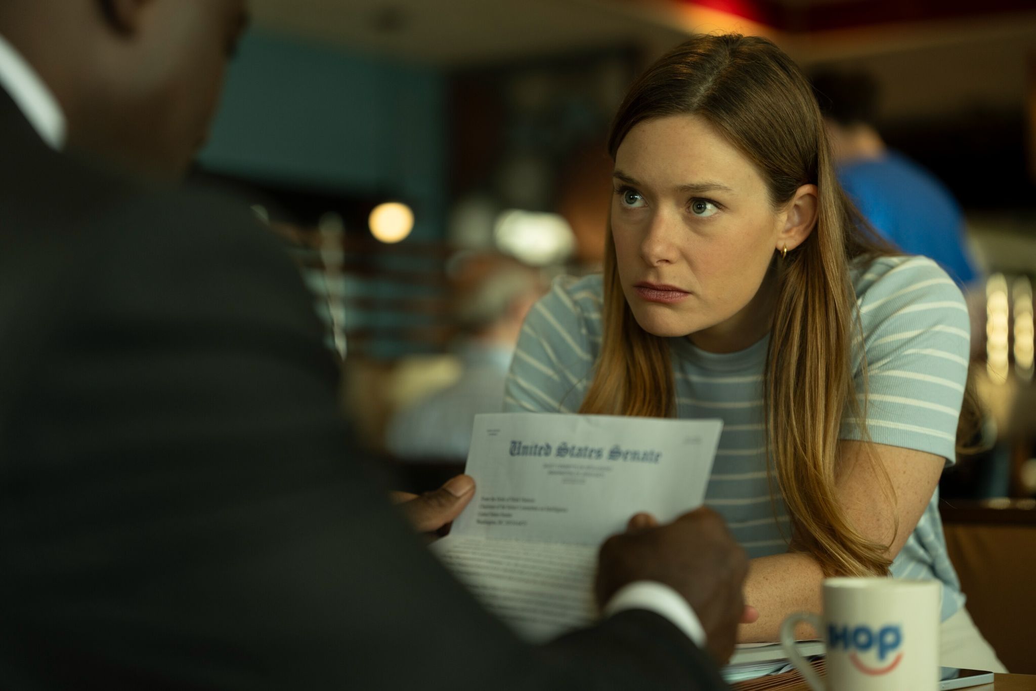 Rachel Keller as Olivia Siffre, leaning across a table in an official Cupertino production photograph.