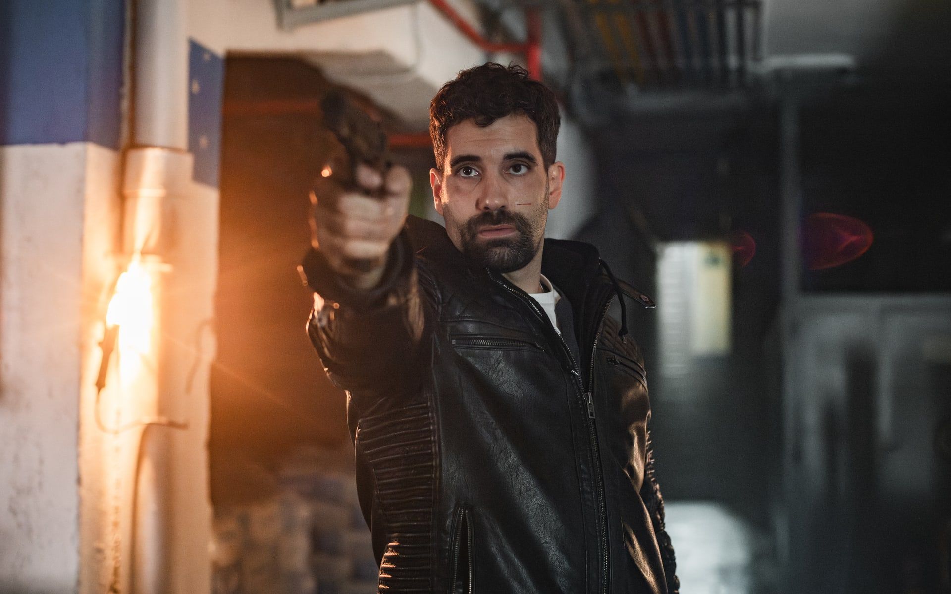 A man in a dark jacket stands beside flames in an official still from Collision Course.