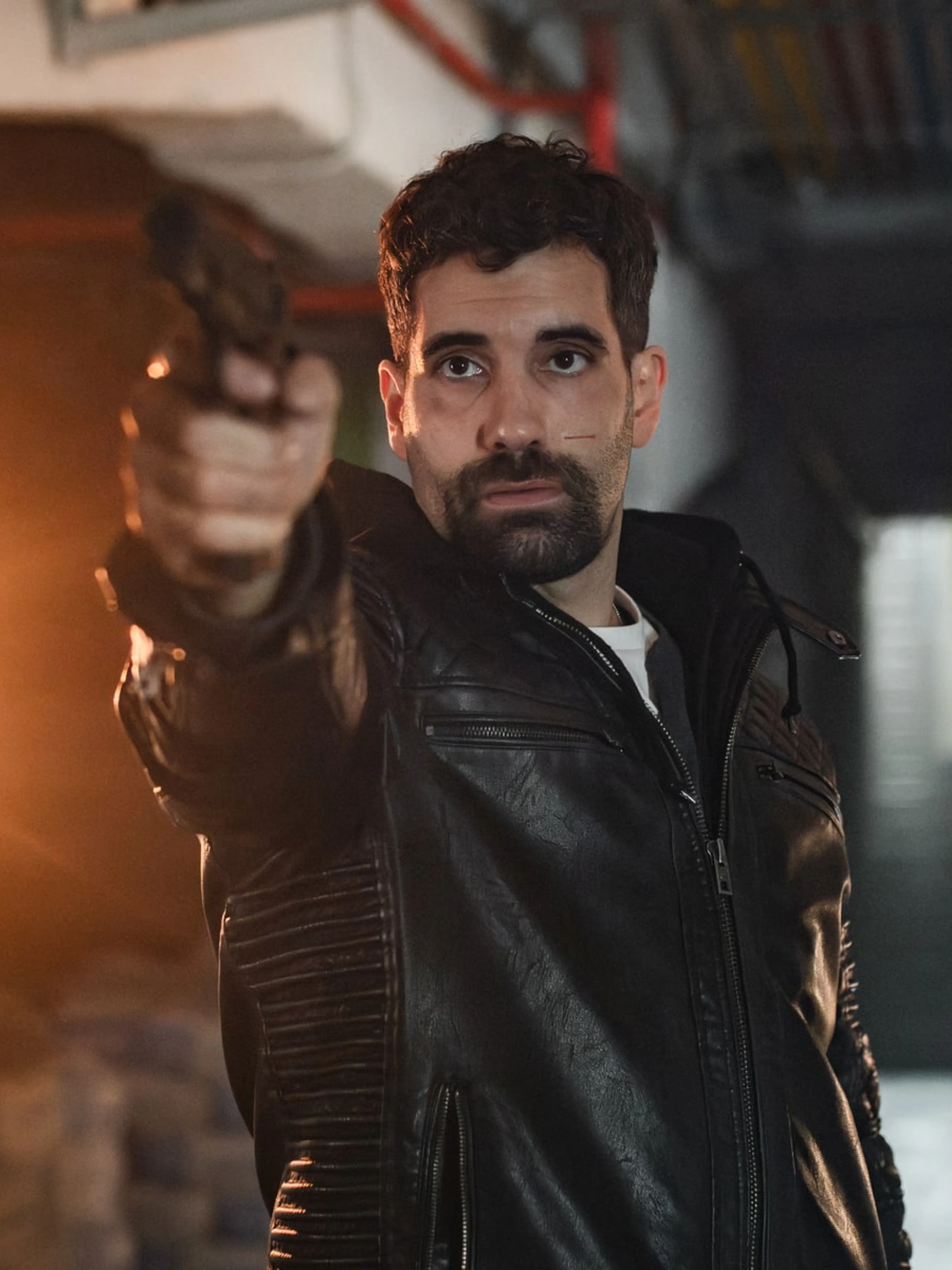A man in a dark jacket stands beside flames in an official still from Collision Course.