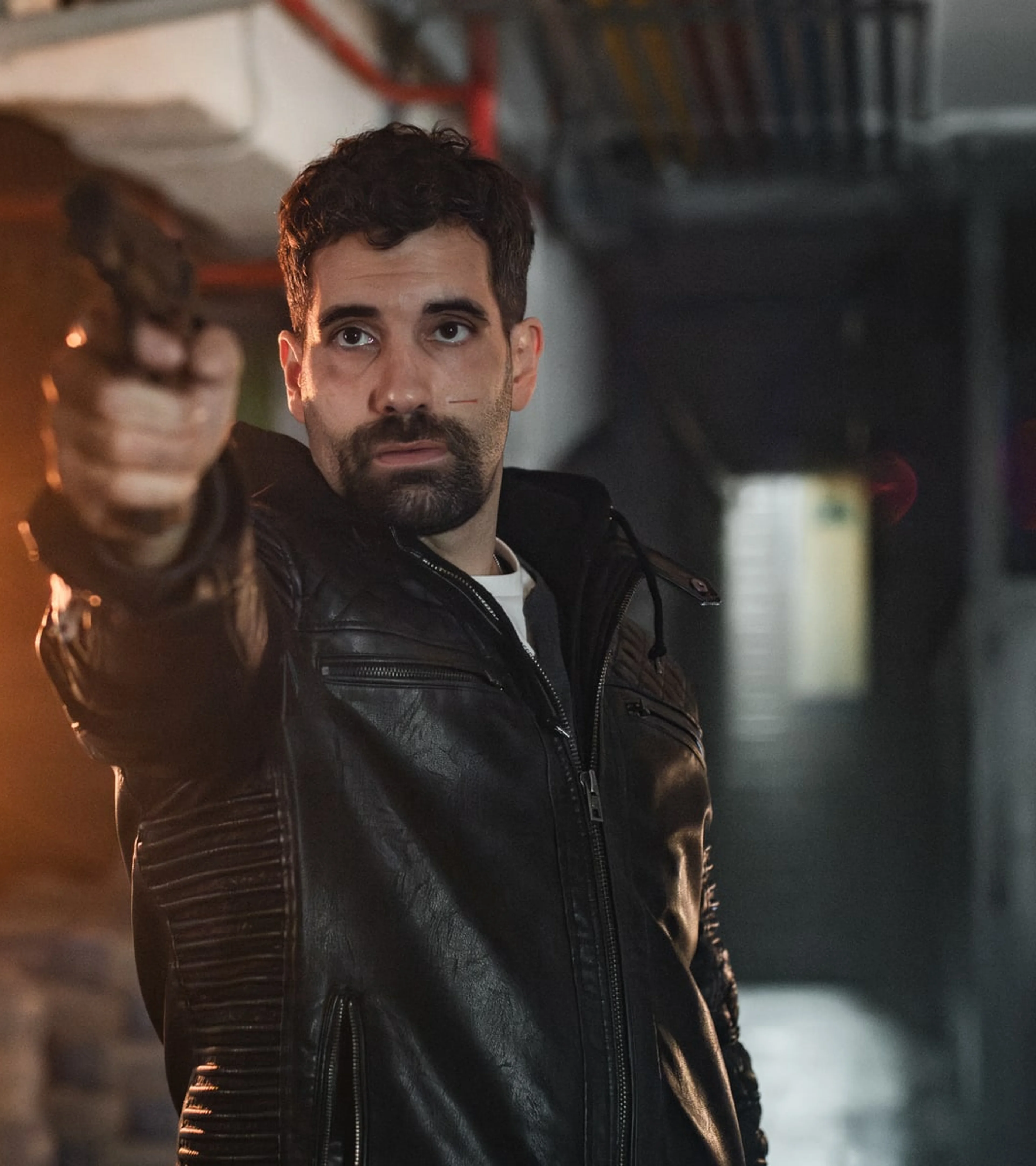 A man in a dark jacket stands beside flames in an official still from Collision Course.