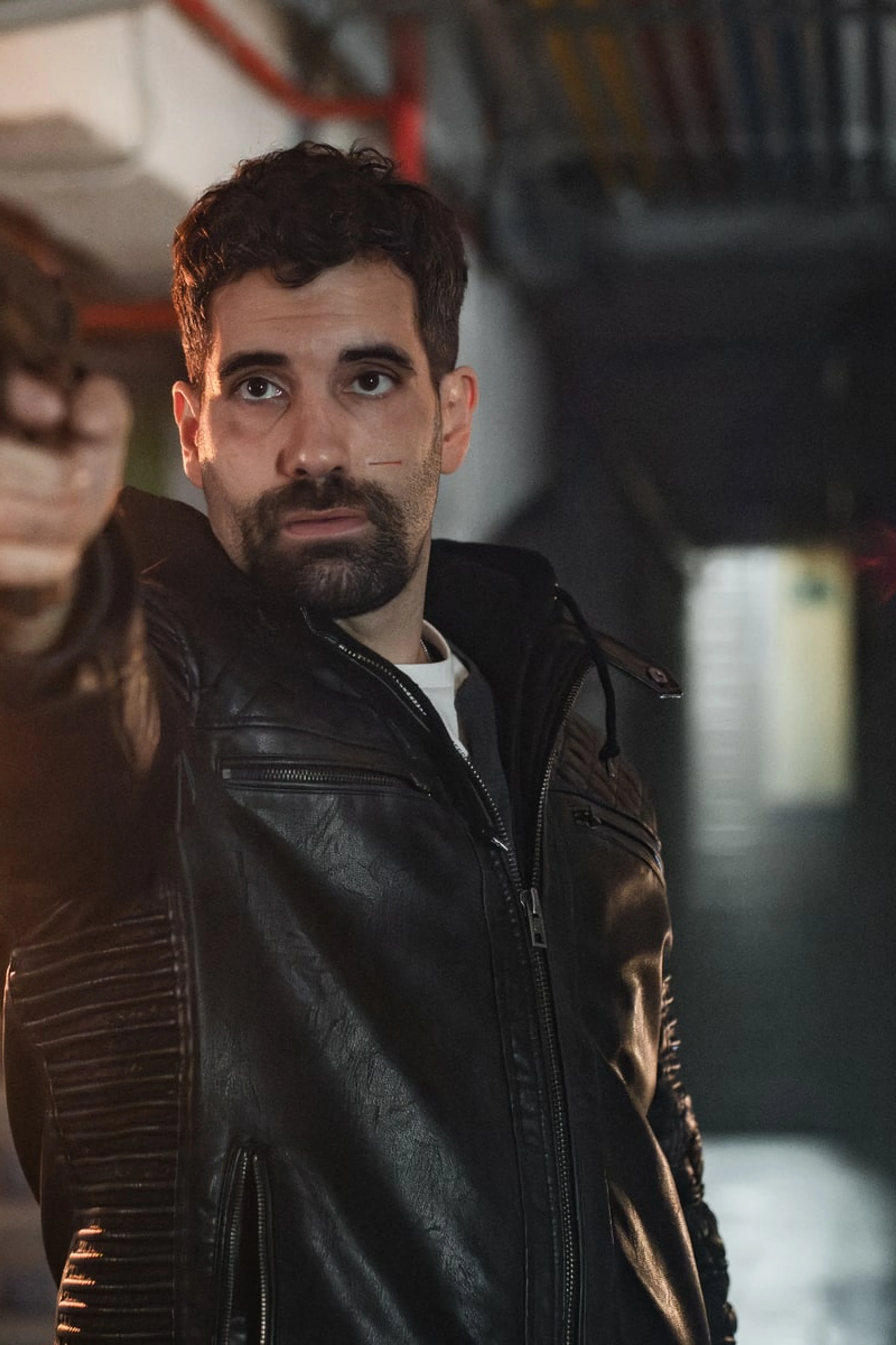 A man in a dark jacket stands beside flames in an official still from Collision Course.