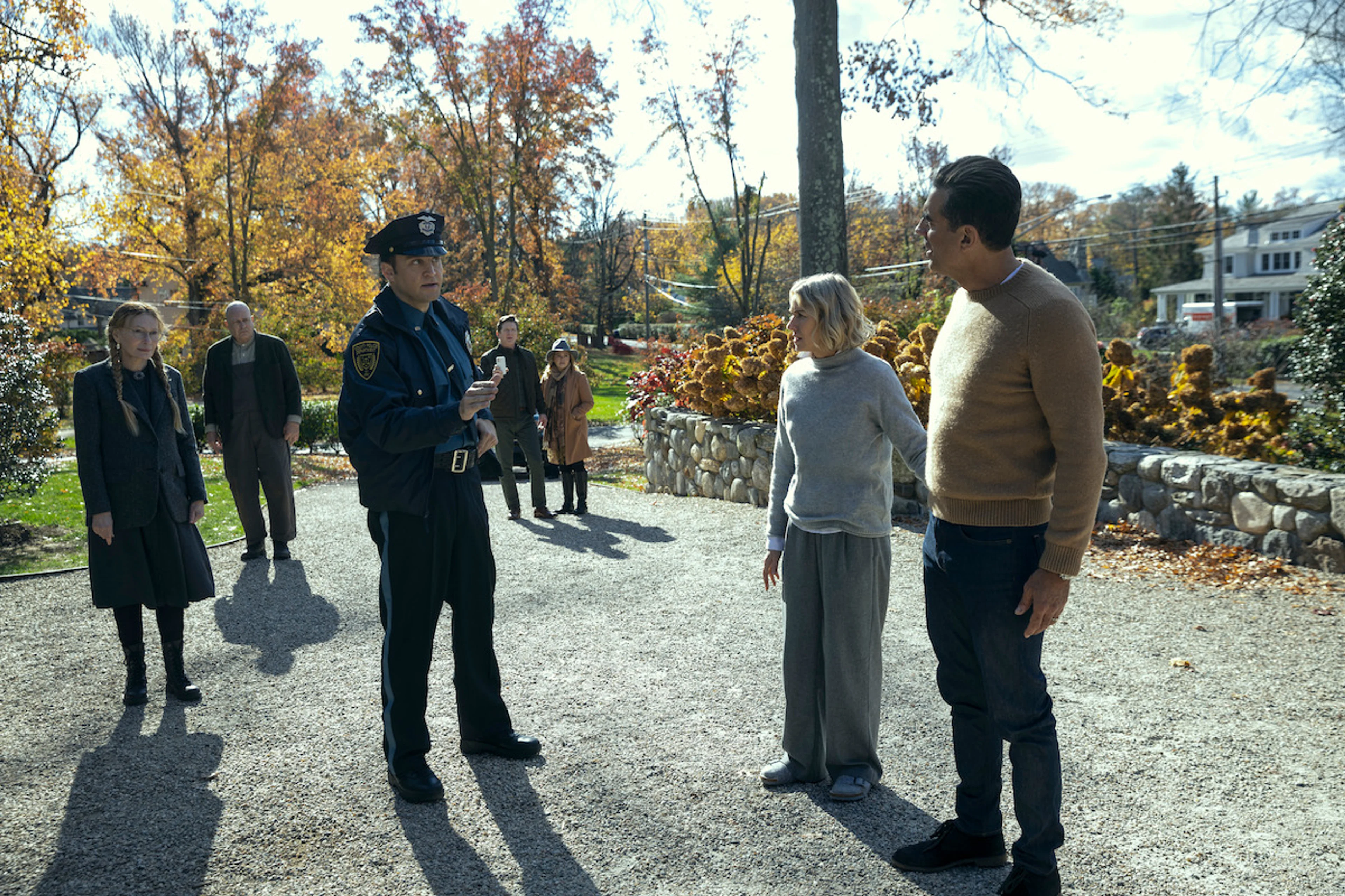 Dean and Nora speak to a police officer with neighbors nearby in The Watcher Season1.