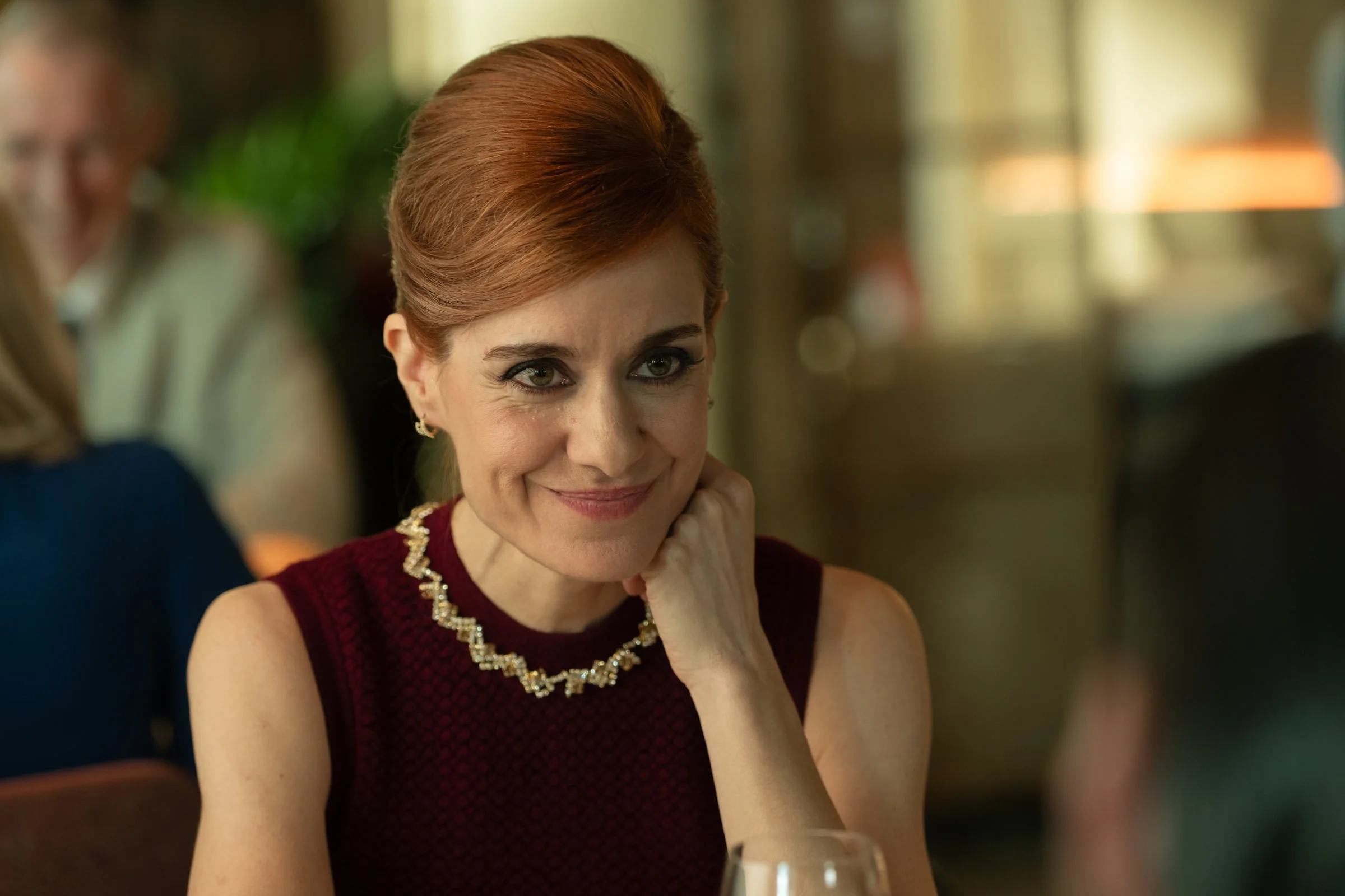 Sofía Carrington sits in an elegant room wearing a red-brown dress and necklace.