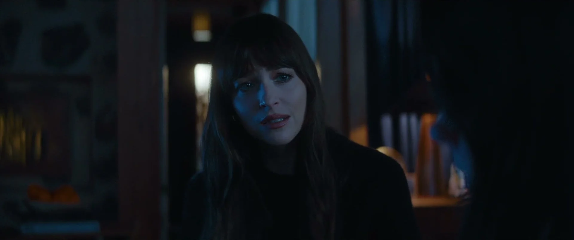 Lowen faces Verity in a dark room, with her mouth slightly open as she speaks.