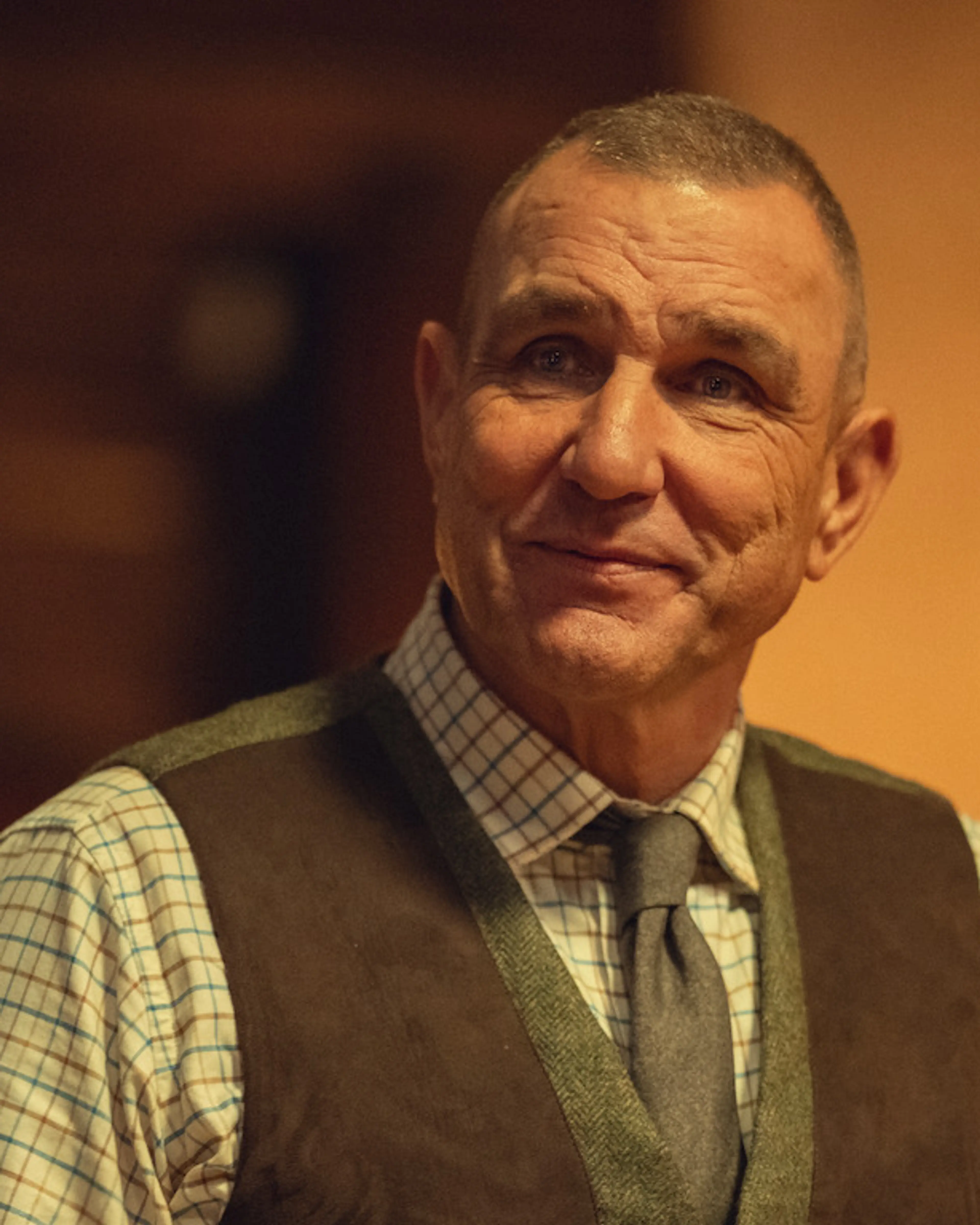 Vinnie Jones as Geoff Seacombe holds an open book while wearing a checked shirt and waistcoat.