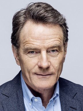 Bryan Cranston in a dark blazer and blue shirt against a pale gray background.