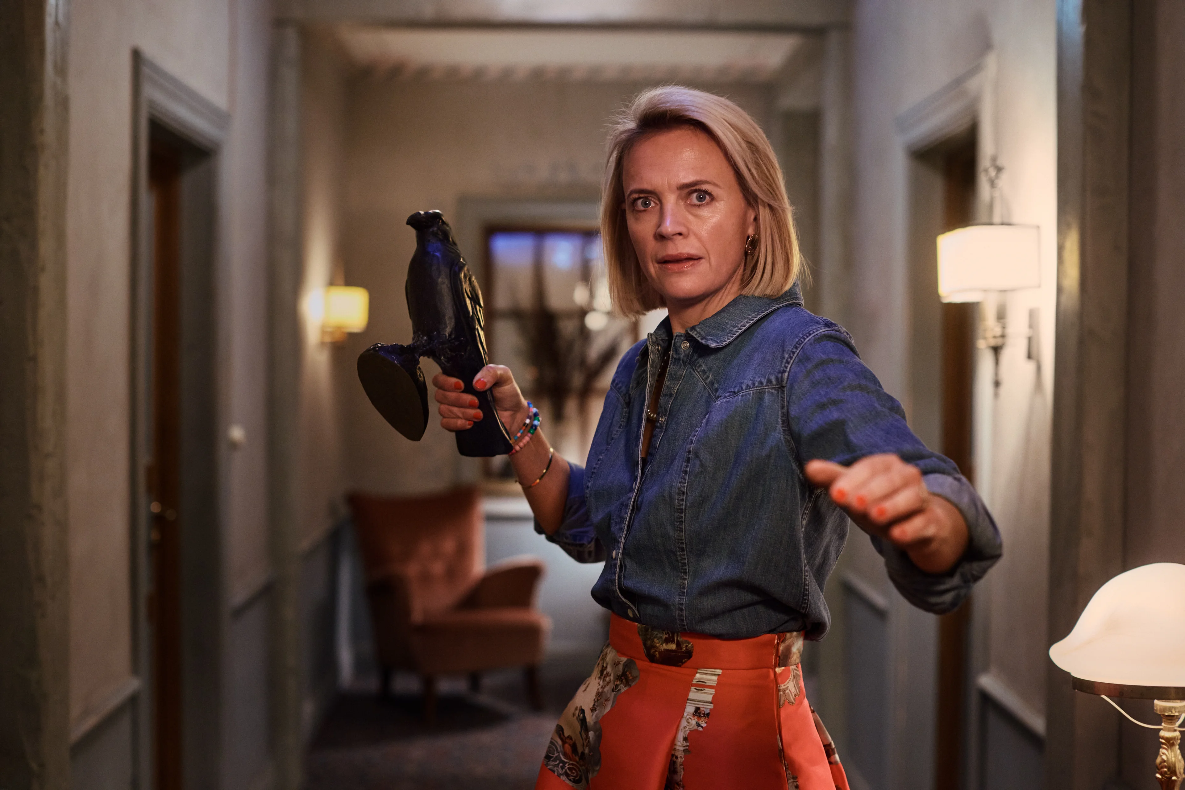 A woman holding an appliance looks alarmed in a farmhouse hallway.