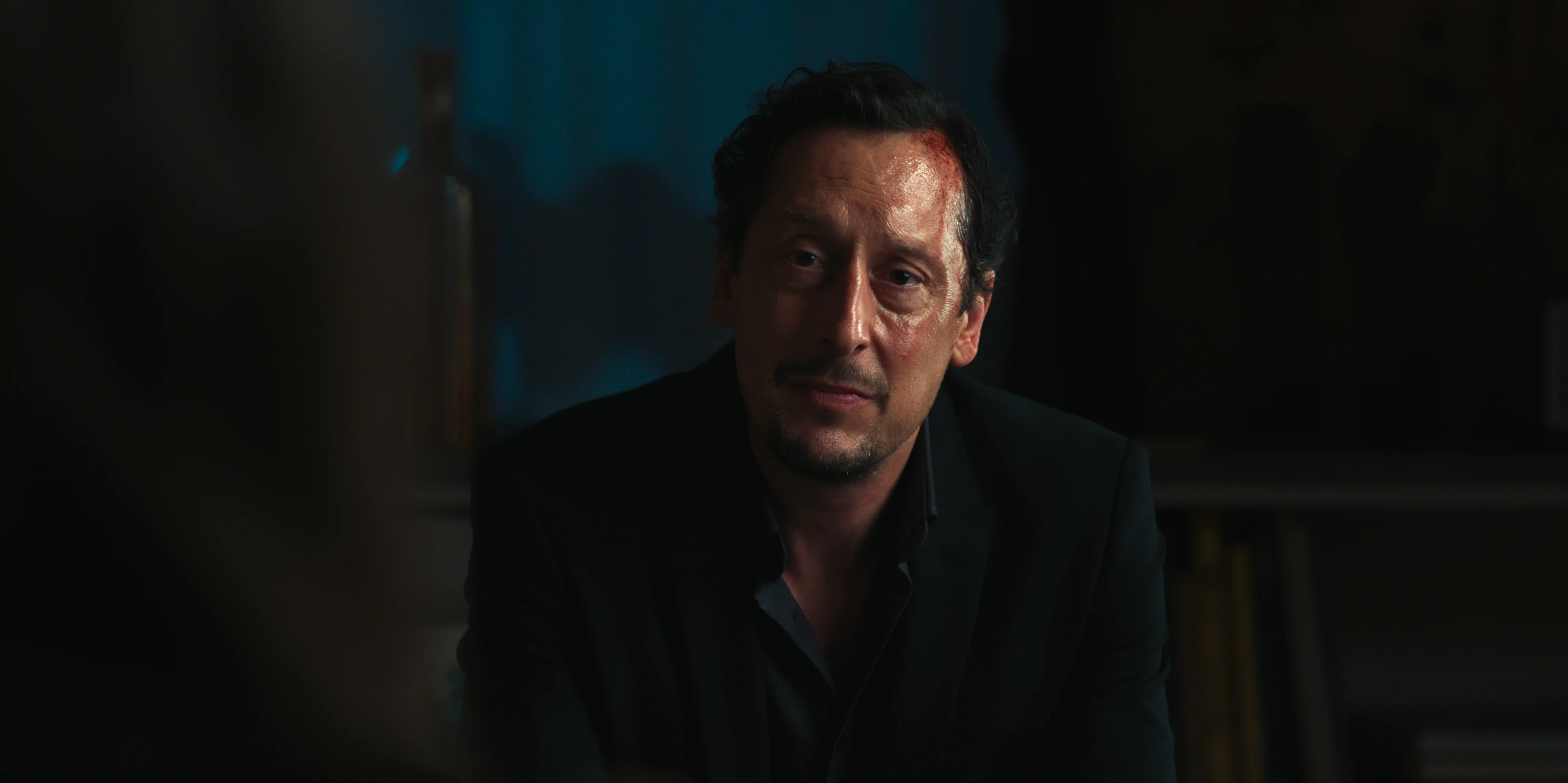 Hans Löw as Robert Lenzen sits opposite a woman in a dim room.