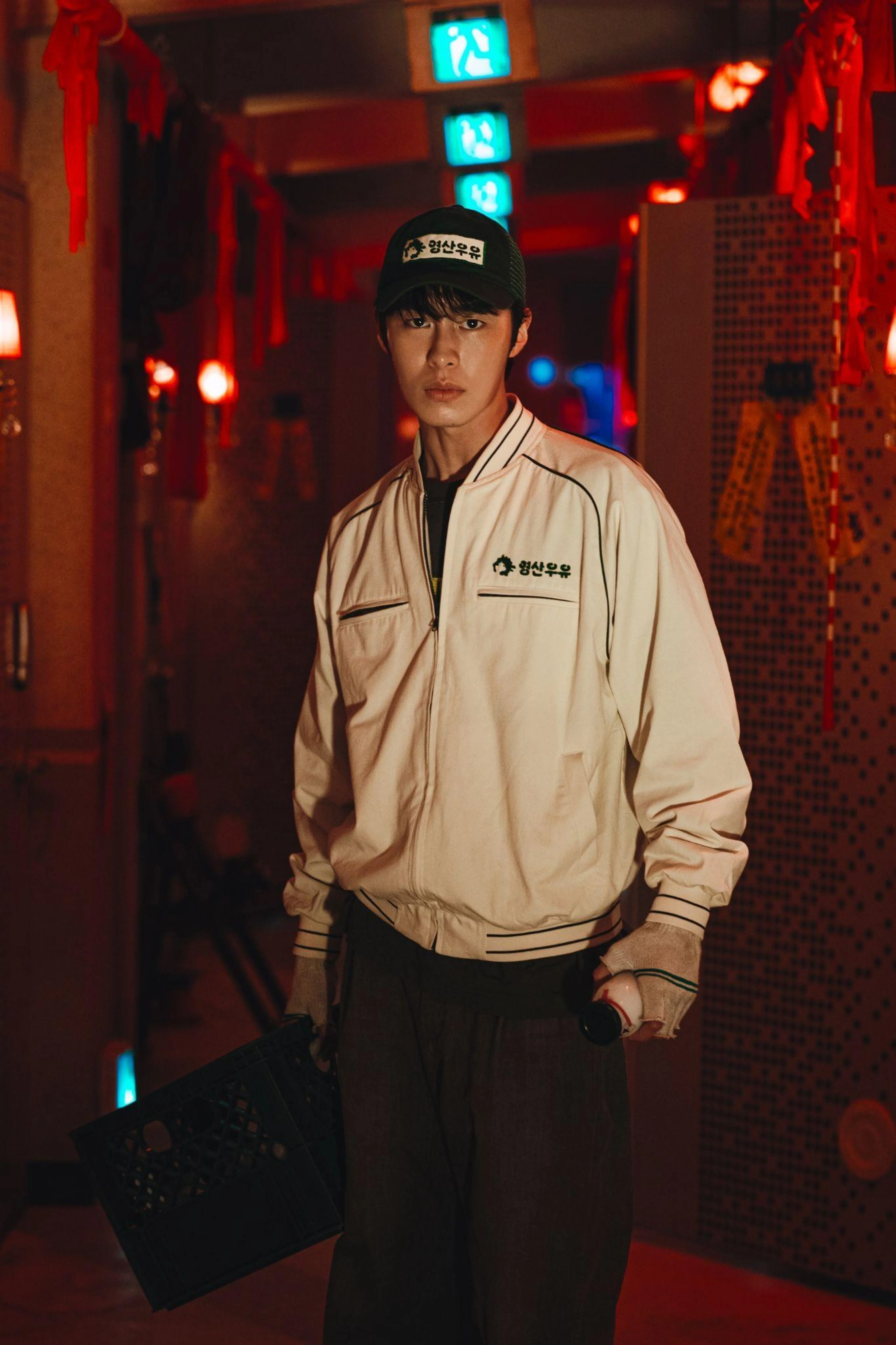 A young man in a work uniform stands in a red-lit interior.