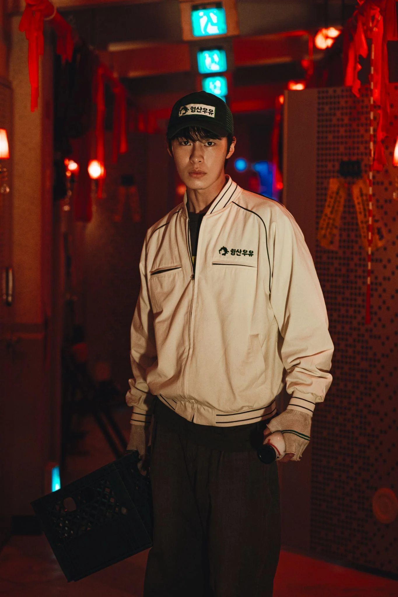 A young man in a work uniform stands in a red-lit interior.