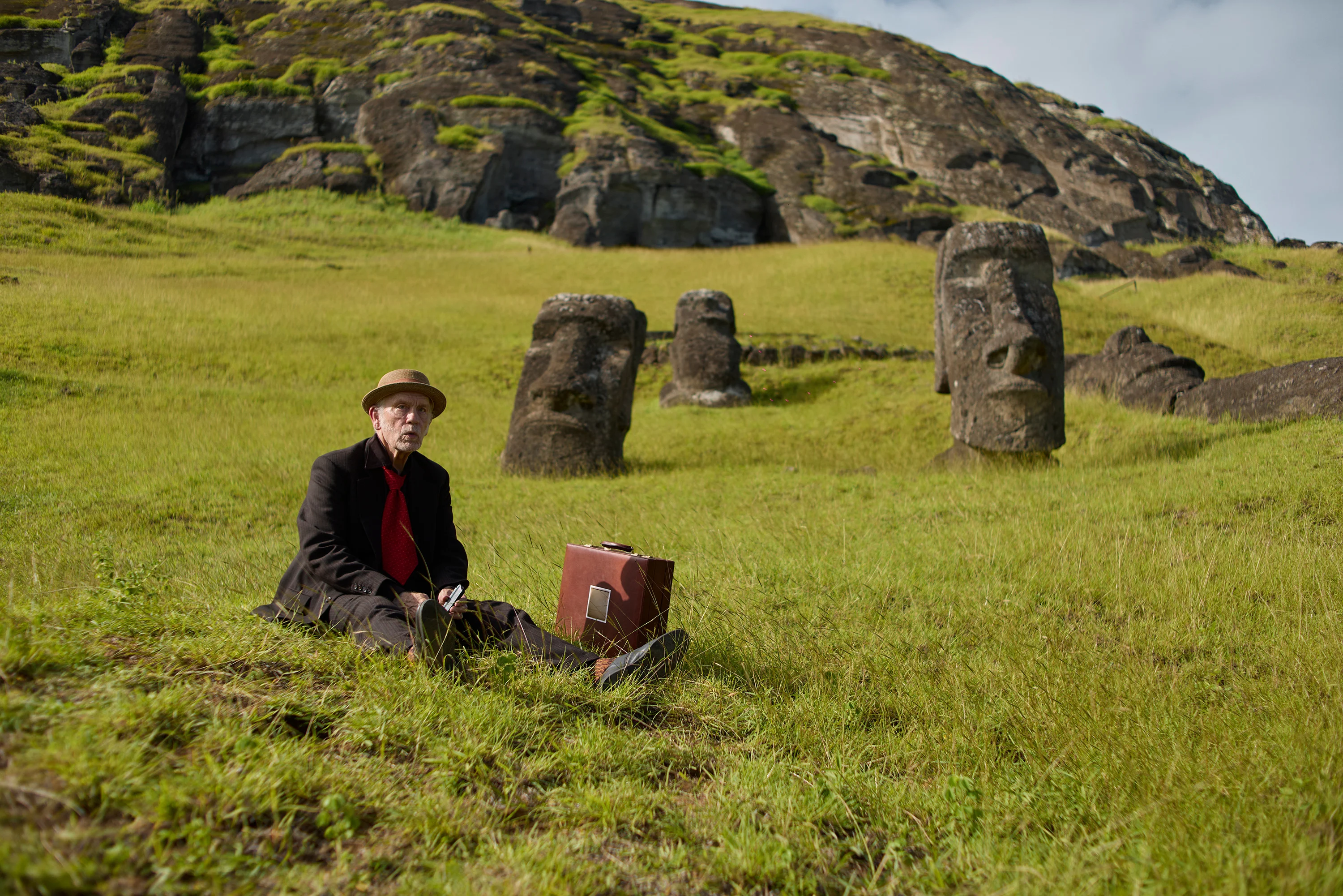 John Malkovich sits in a field near moai statues on Rapa Nui in Wild Horse Nine.