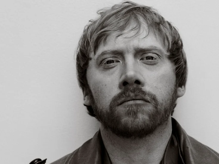 Rupert Grint looks into the camera in a black-and-white portrait.