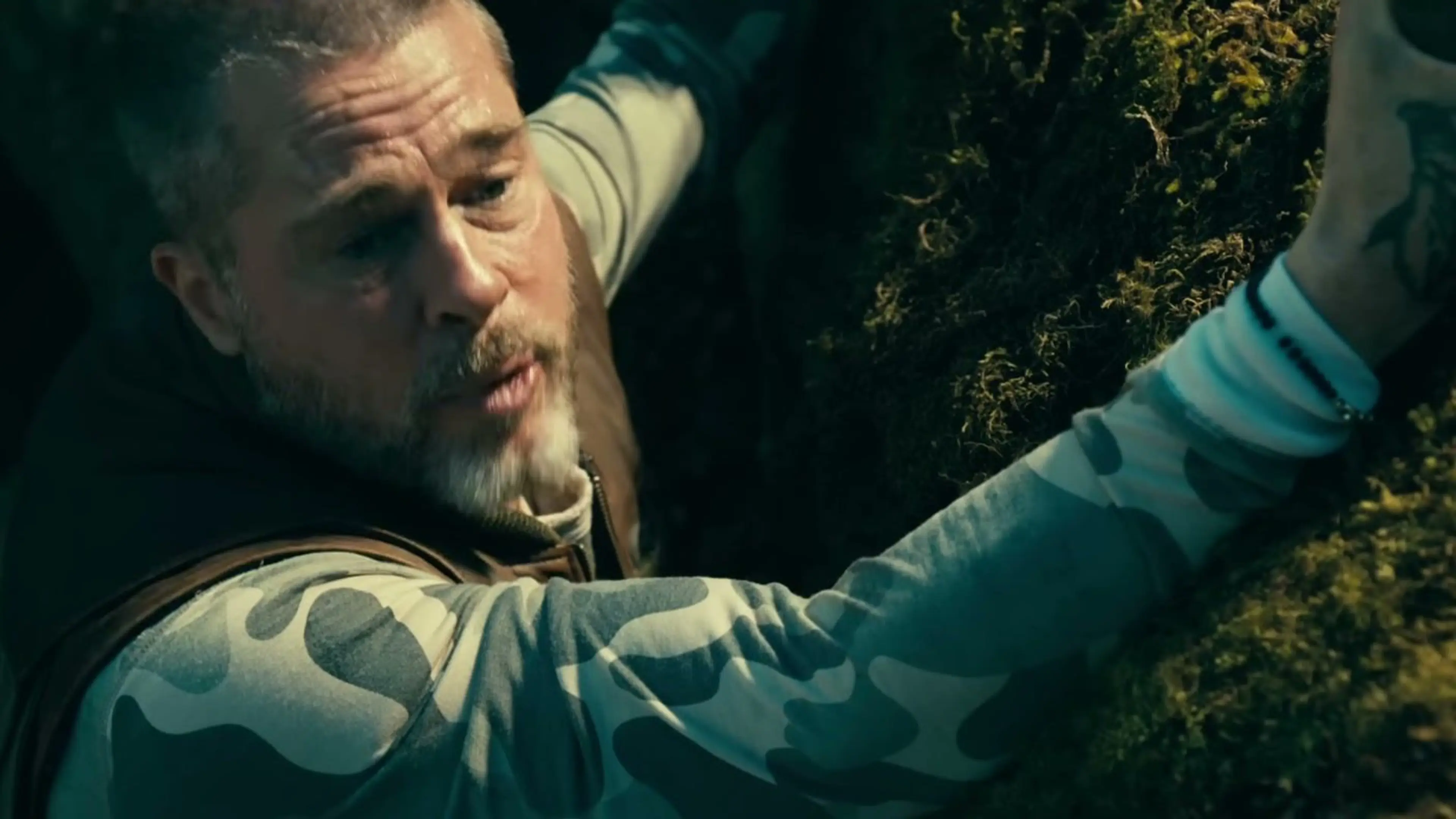 James grips a moss-covered rock face with an injured arm.
