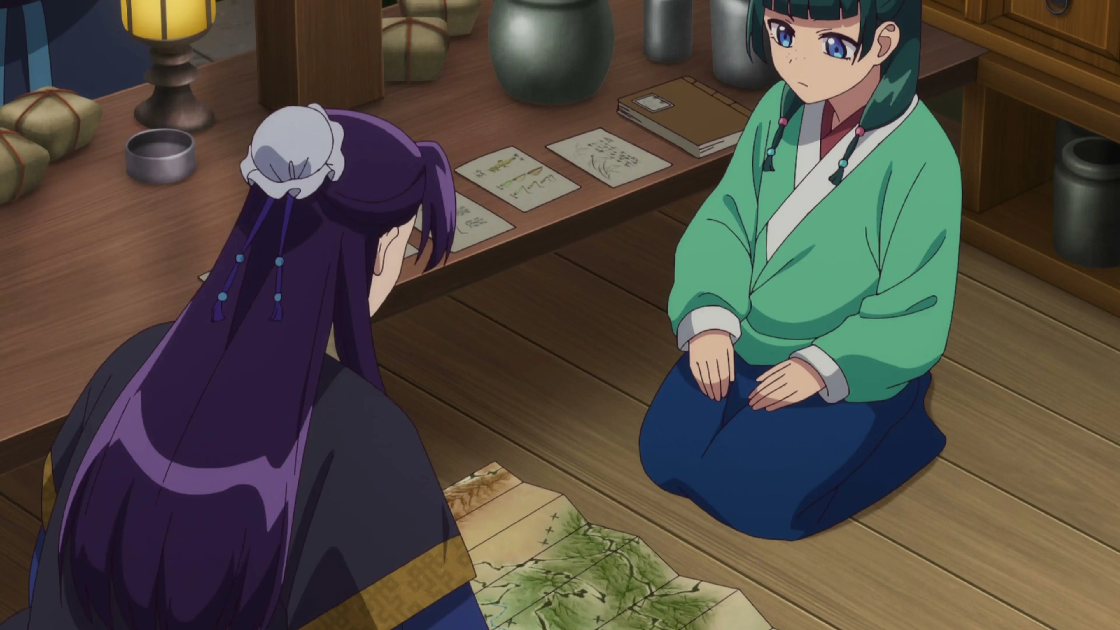 Maomao speaks with Jinshi at a table in the Season 3 trailer.