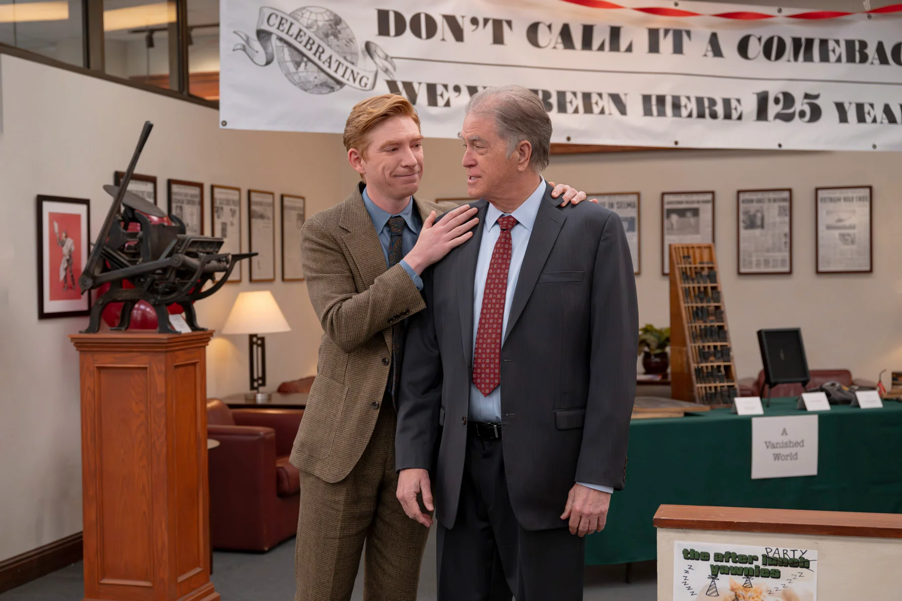 Ned puts his hands on Marv’s shoulders beneath the newspaper’s 125th-anniversary banner.