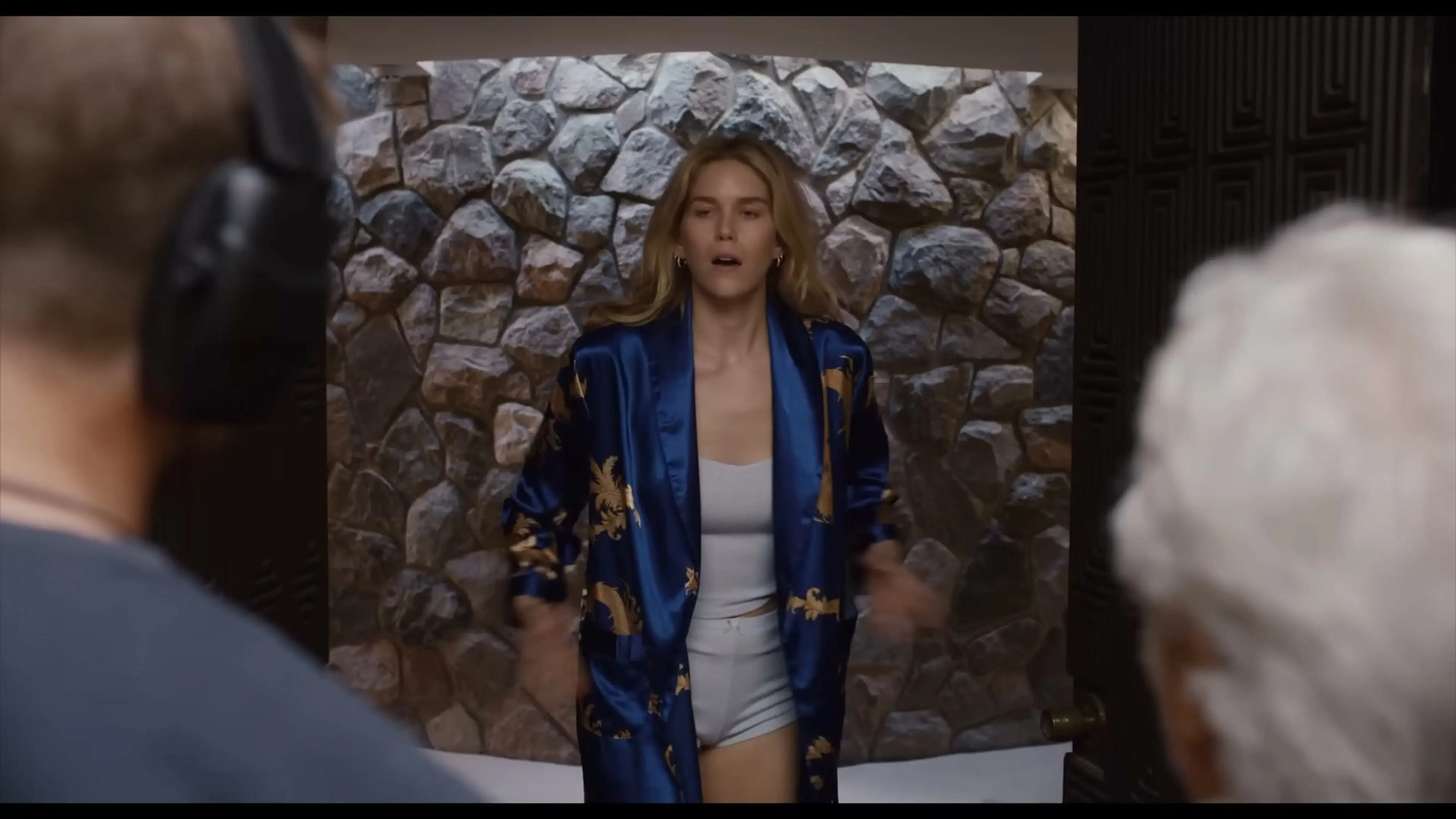A woman in a blue robe greets Niki and Harry at a doorway.