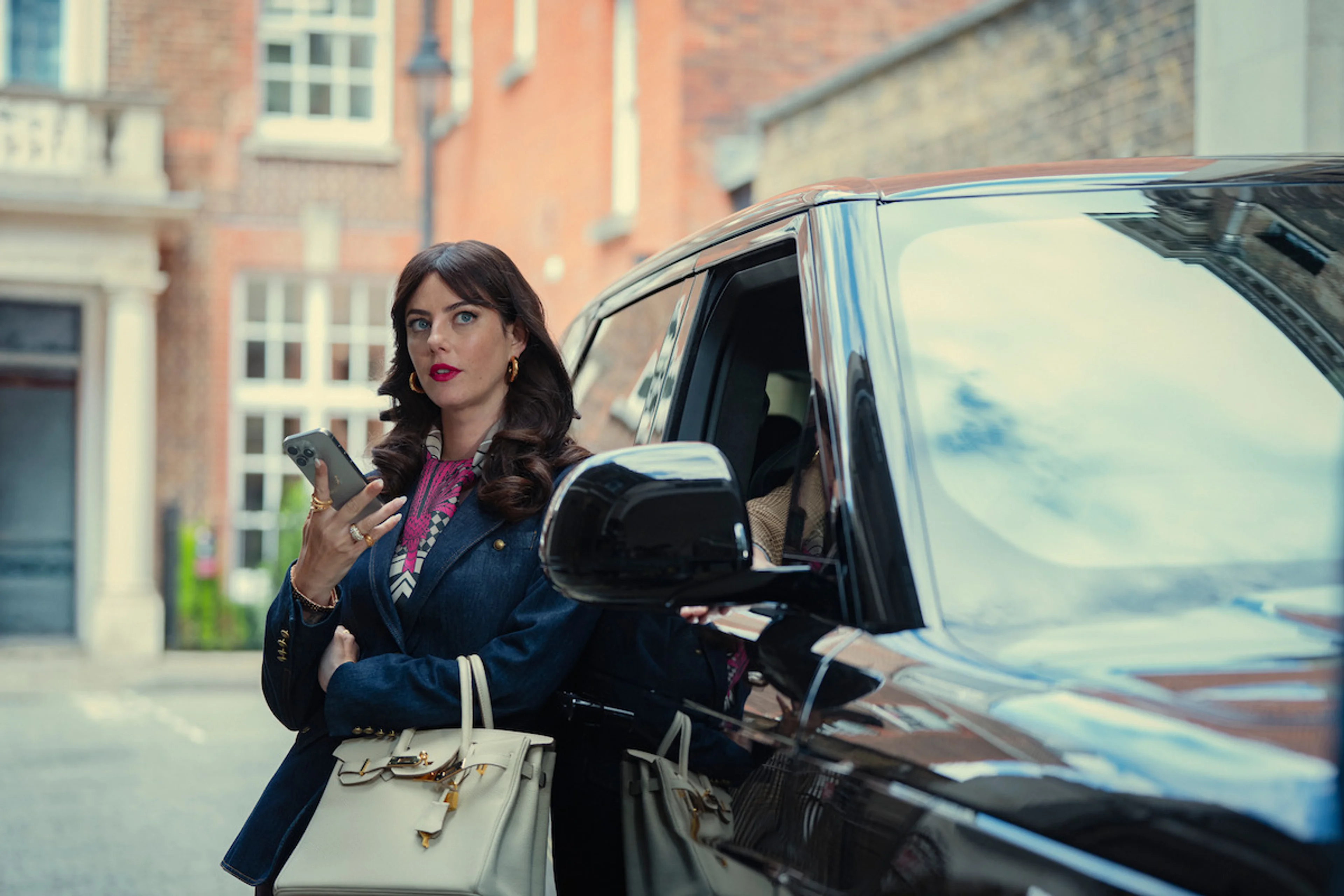 Susie Glass stands beside a black car while handling business in The Gentlemen Season 2.