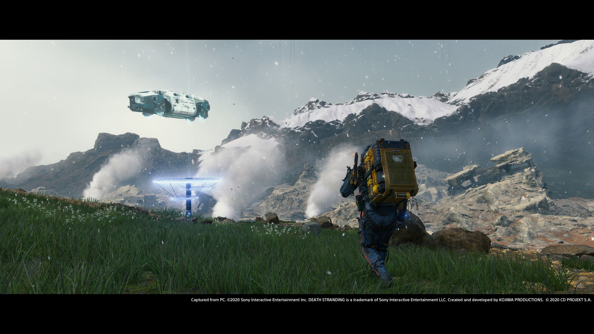 Sam walks through rocky terrain carrying a tall stack of cargo.
