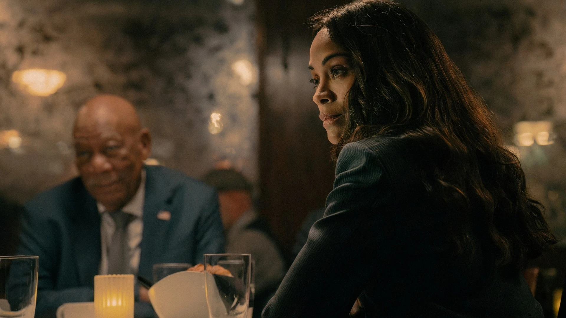 Zoe Saldaña as Joe sits at a table with Morgan Freeman as Edwin Mullins in Lioness Season 3.
