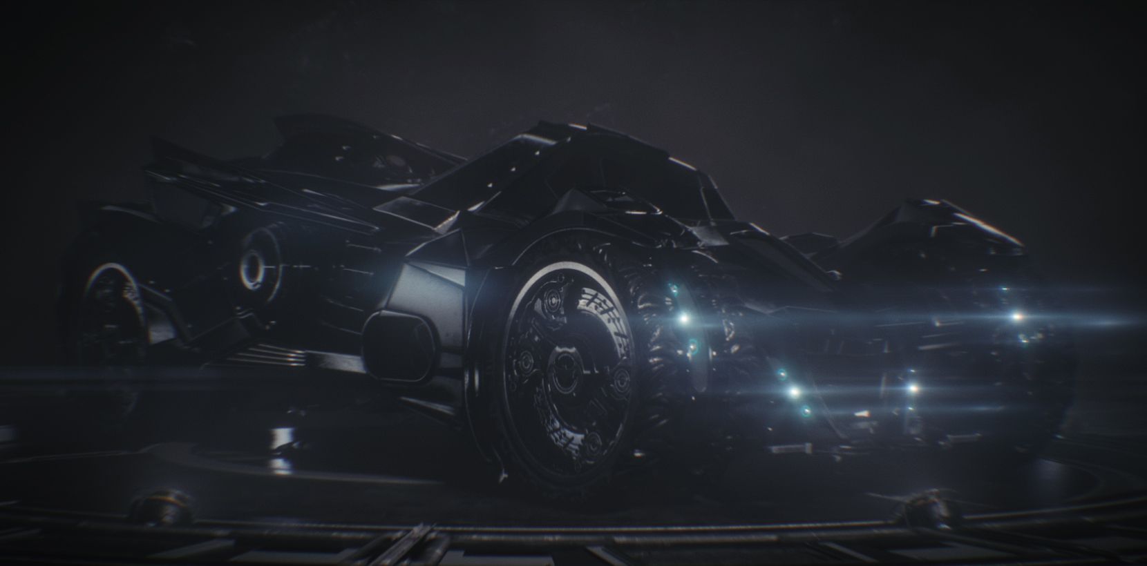 The Batmobile sits in a dark garage with its headlights on.
