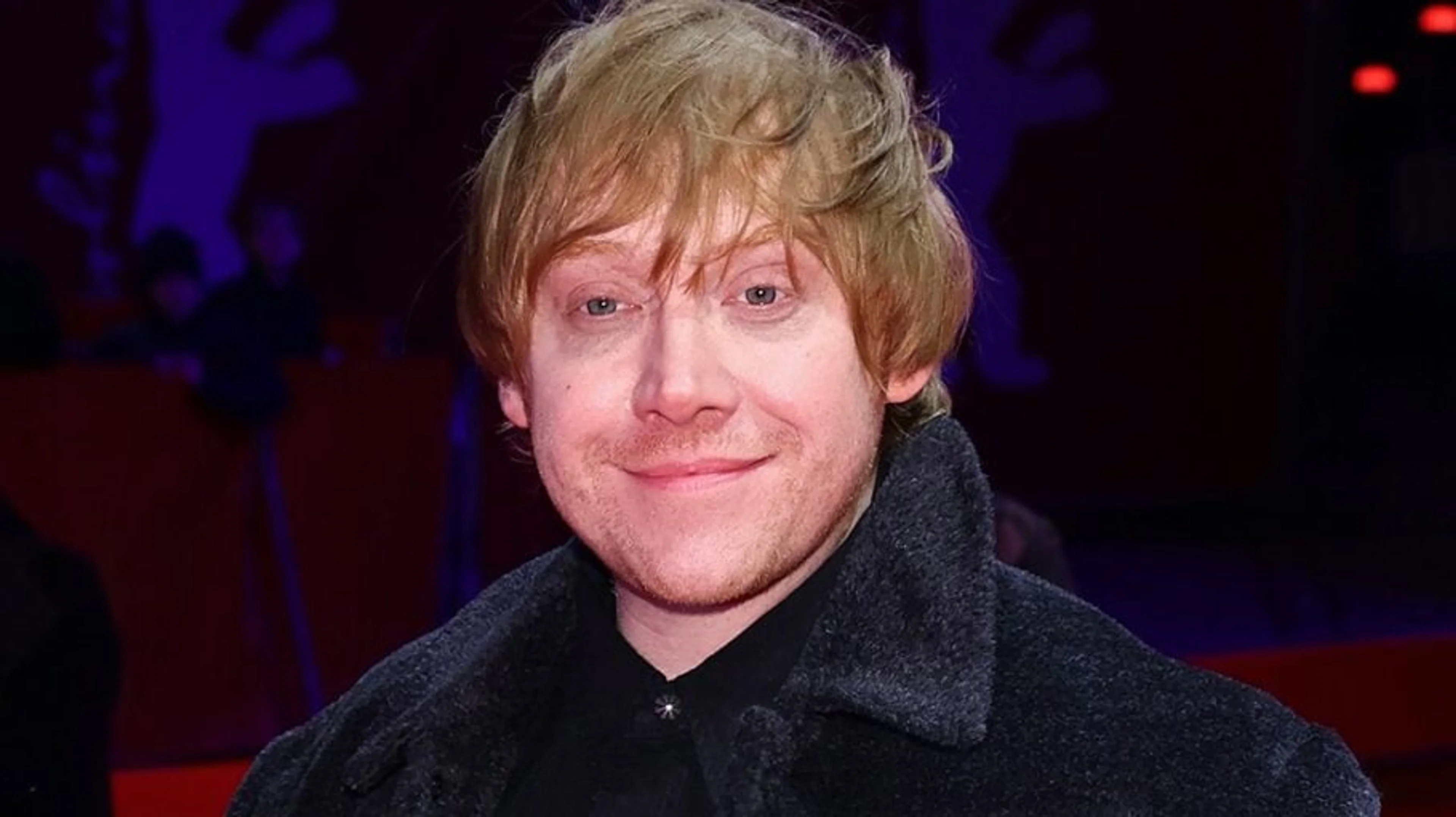 Rupert Grint smiles at a premiere in a dark coat.