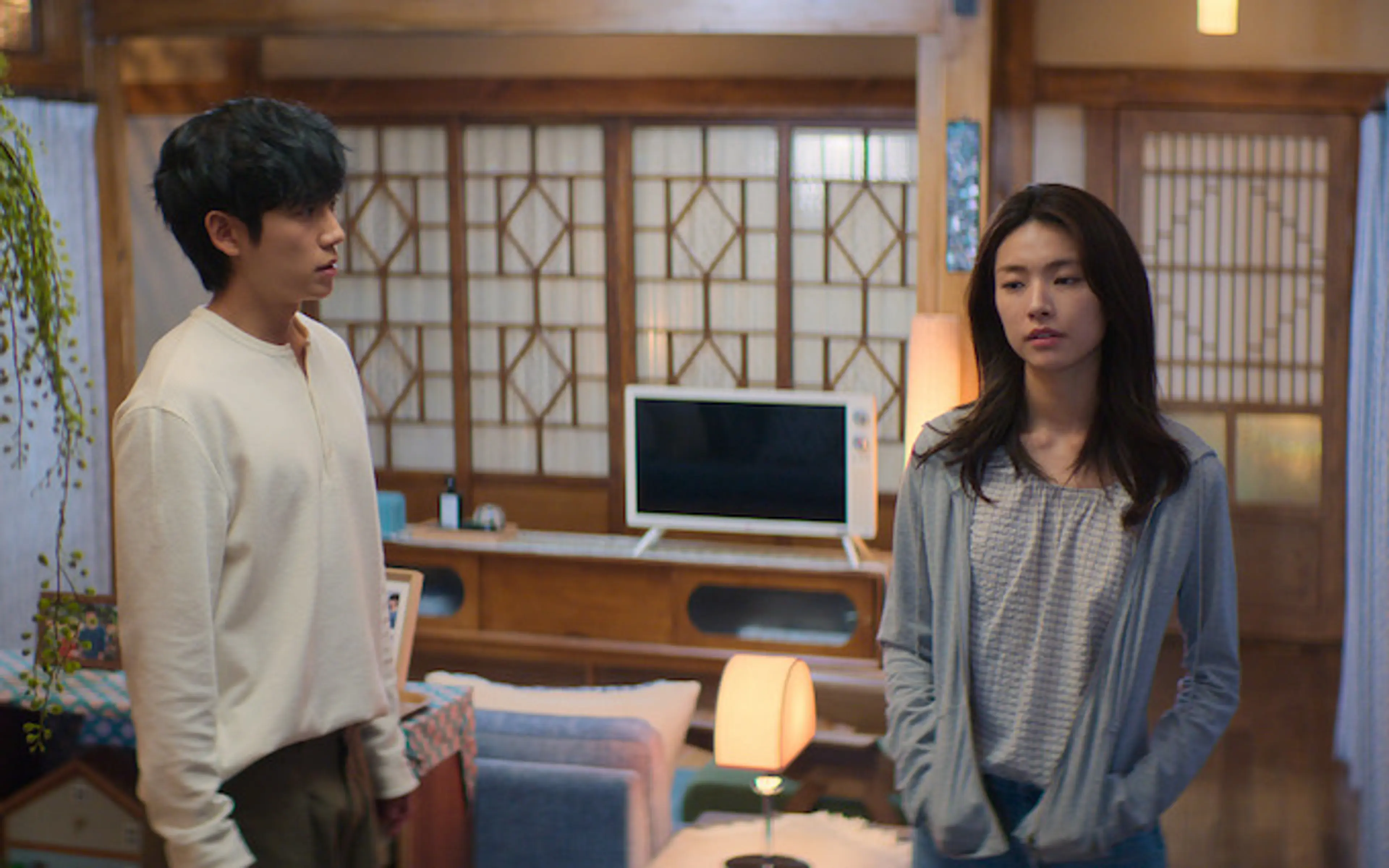 Jung Hae-in and Ha Young stand facing each other in a bedroom with wooden window frames.