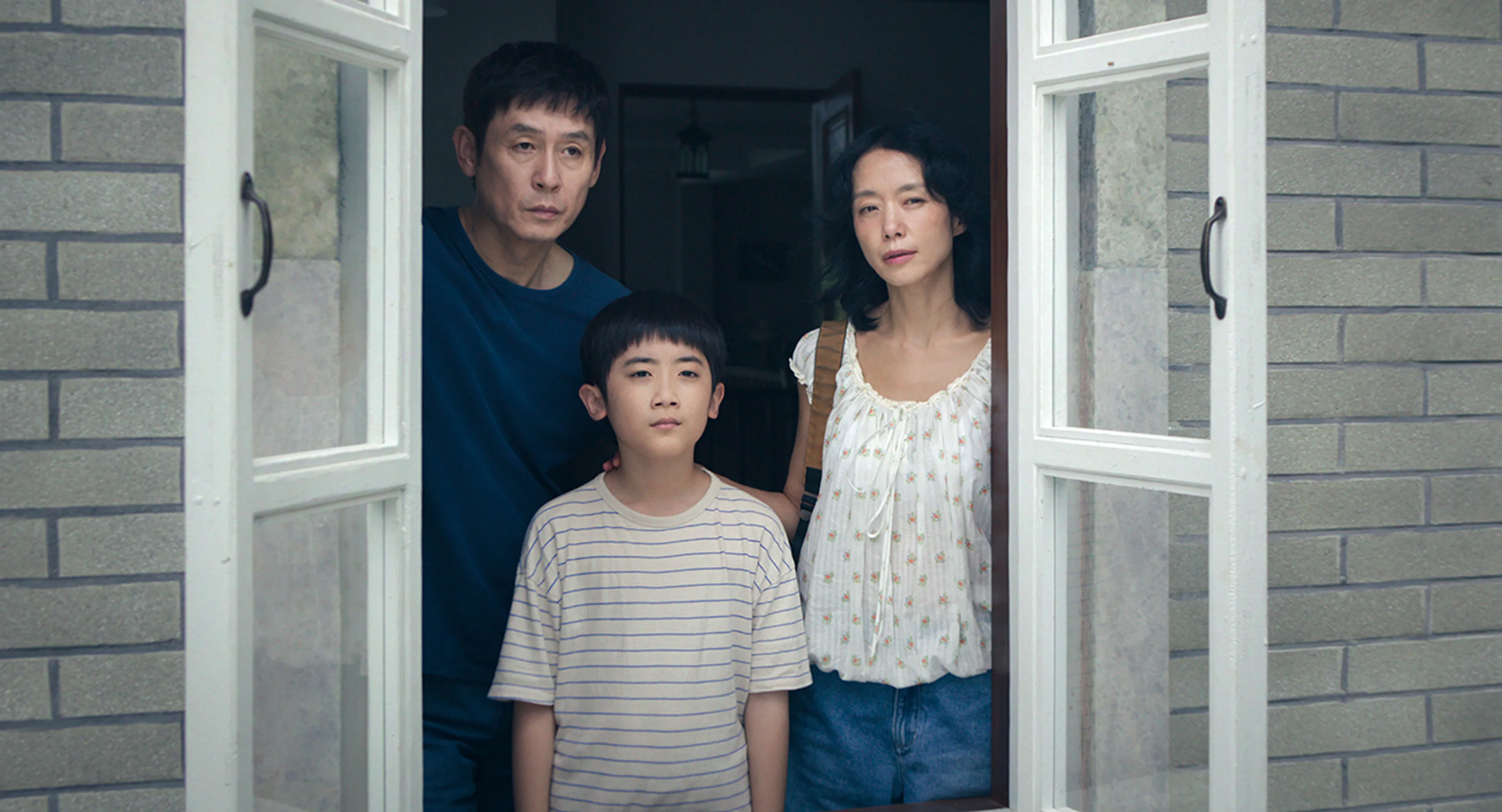 Ho-seok and Mi-ok stand behind their son Cheol at an open window.