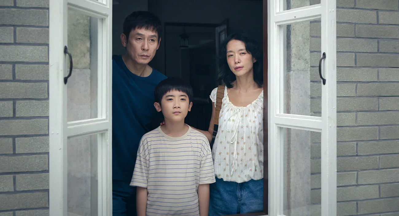 Ho-seok and Mi-ok stand behind their son Cheol at an open window.