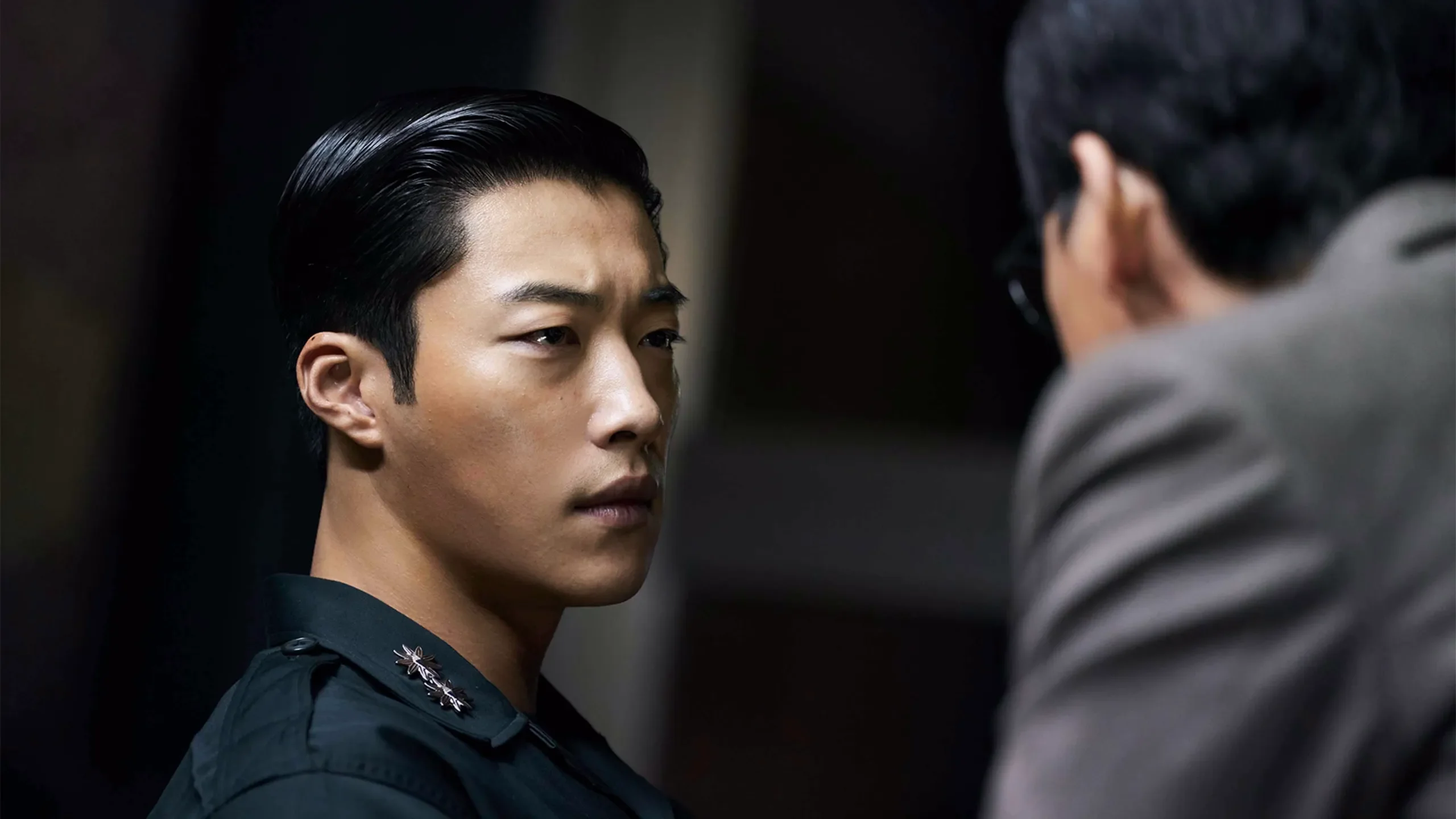 Woo Do-hwan as Ki-hyun looks toward another man while wearing a dark military uniform.