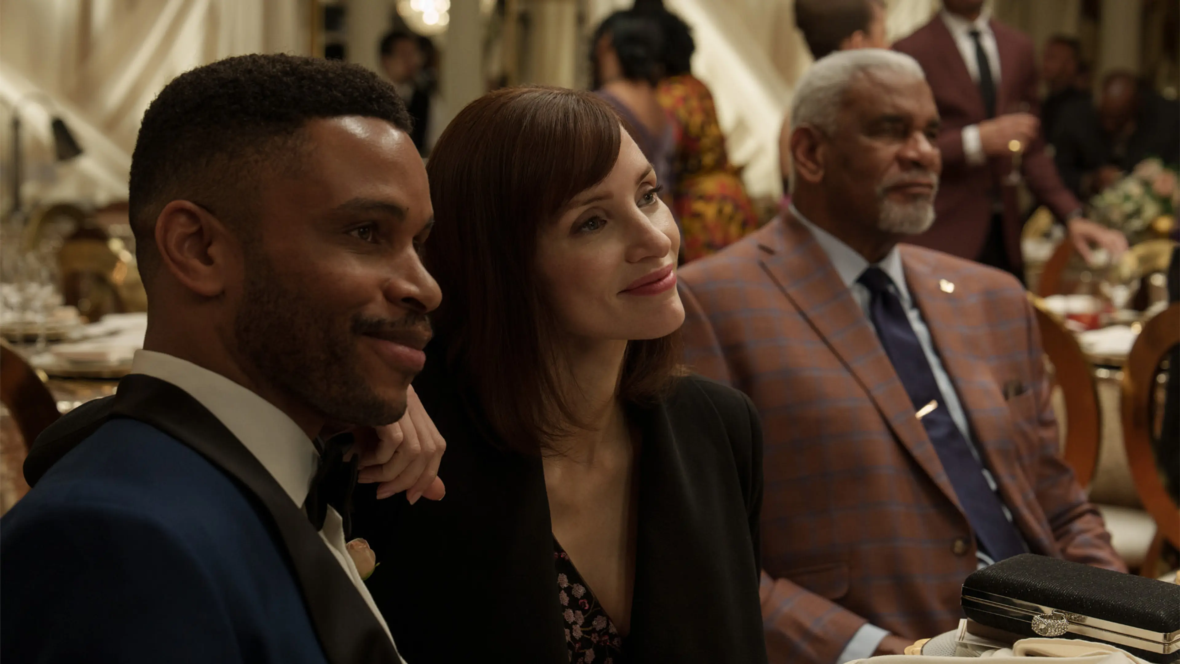 Jessica Chastain sits between two men during a formal event in The Savant.