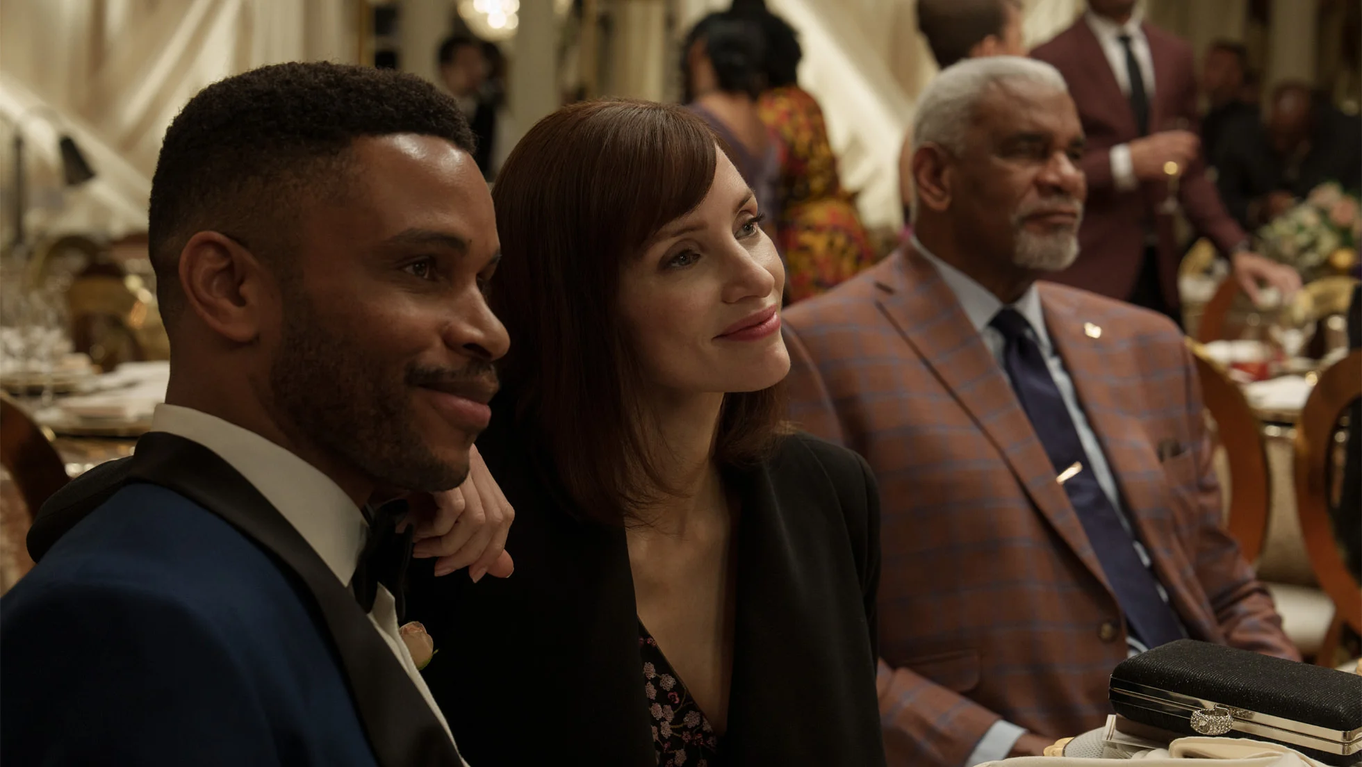 Jessica Chastain sits between two men during a formal event in The Savant.