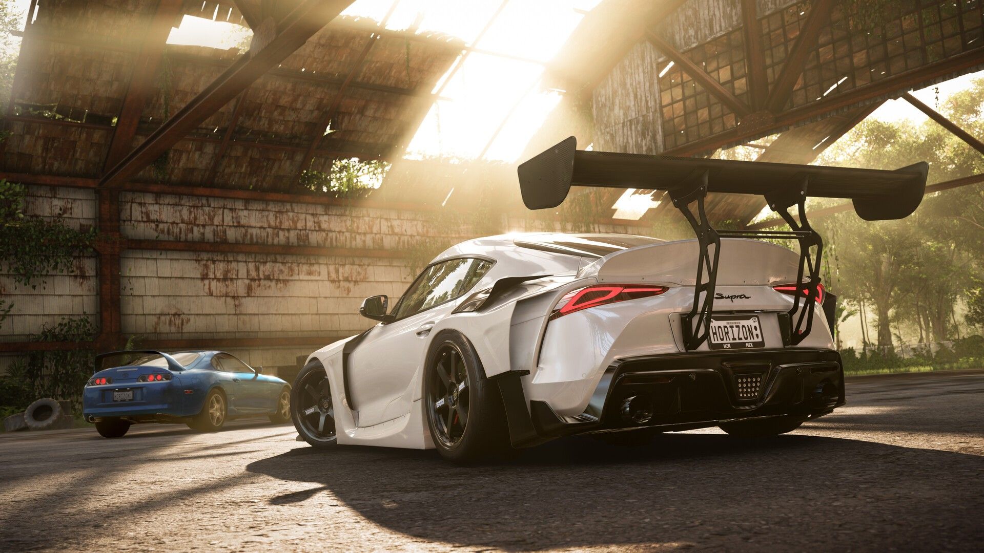 White sports car and blue coupe parked in a sunlit building.