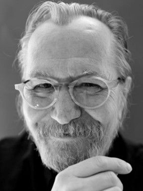 Black-and-white portrait of Gary Oldman smiling with glasses and a beard.